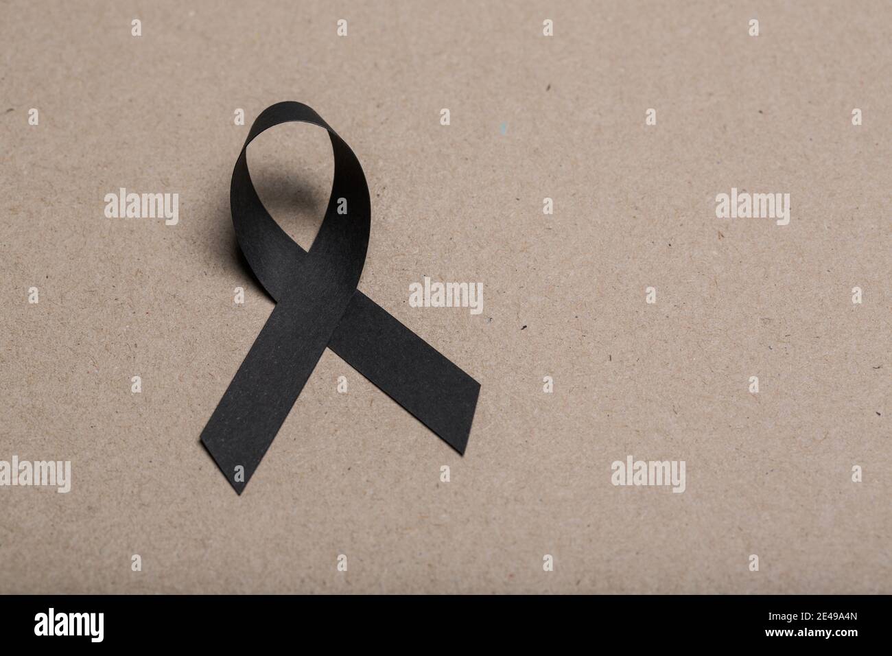 Black handmade awareness paper ribbon on cardboard background. Stock Photo