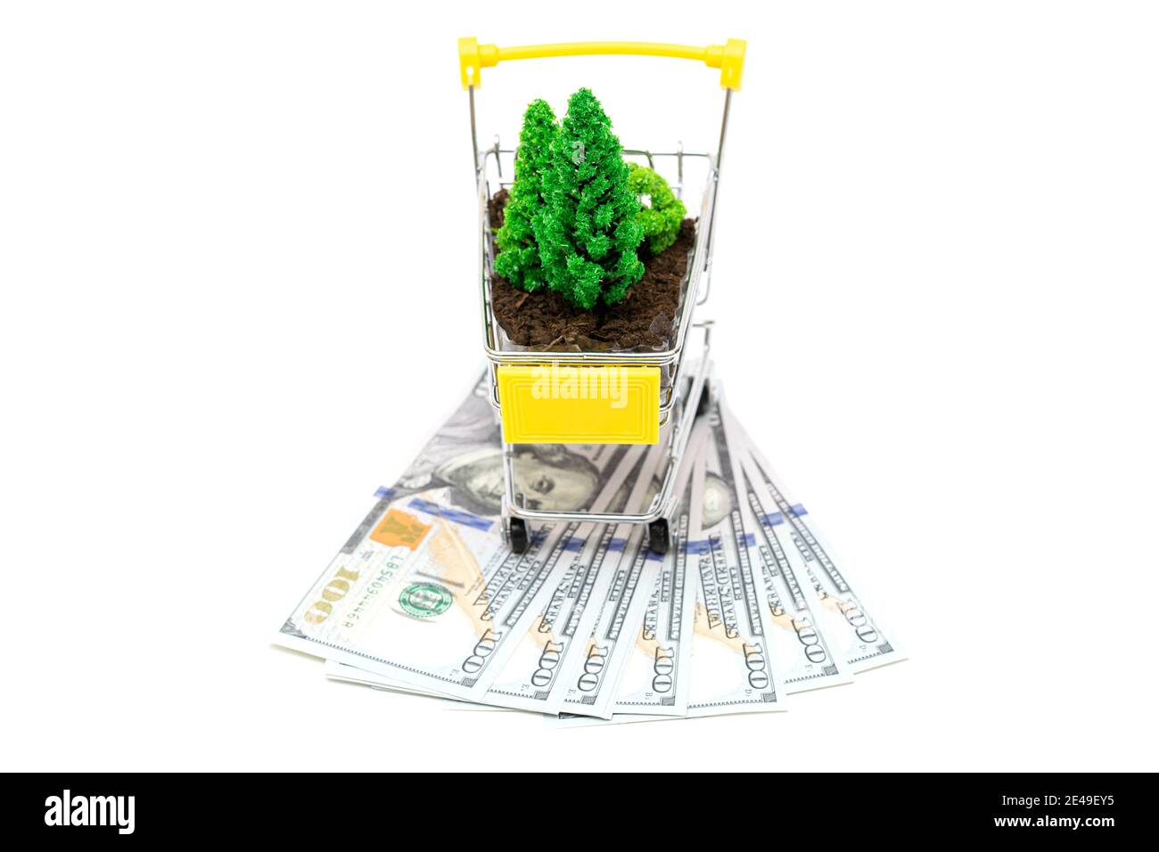 Toy shopping cart with soil and toy trees standing on dollar bills isolated on white. Illegal logging enrichment and deforestation concept. Stock Photo