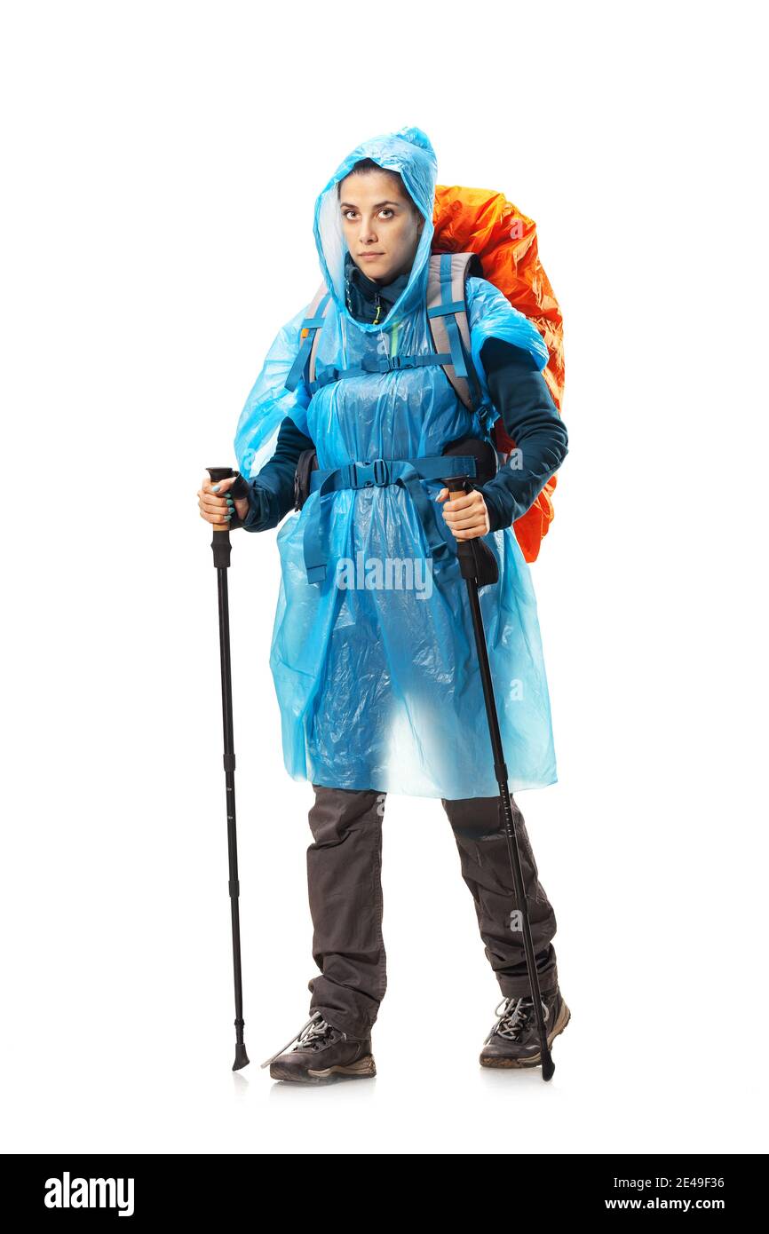 girl with hiking equipment and large backpack, wearing blue raincoat, posing in studio isolated on white. Stock Photo