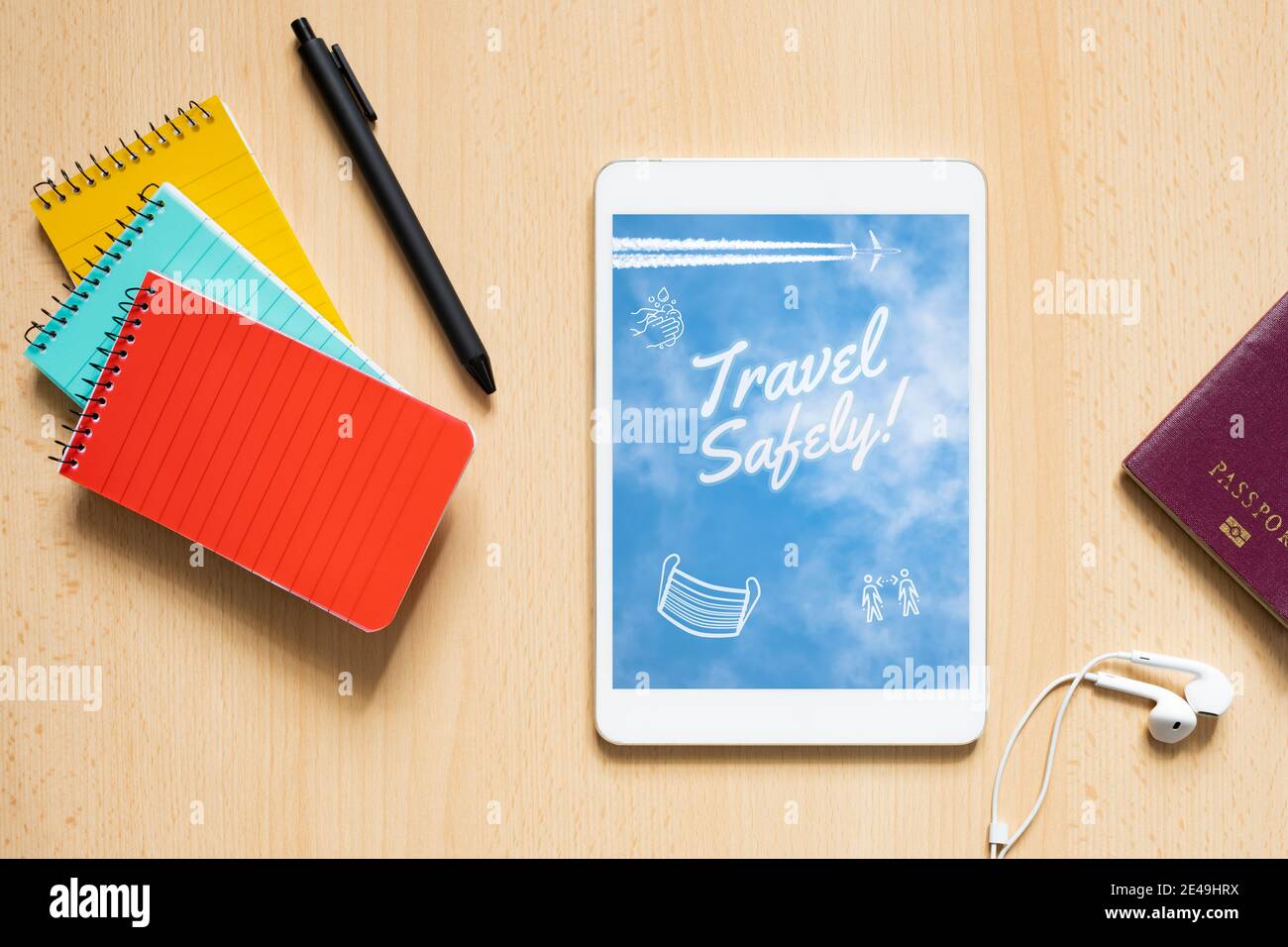 Flat lay with copy space, view from above of three colorful notepads, pen, passport and a tablet with a digital illustration. Stock Photo