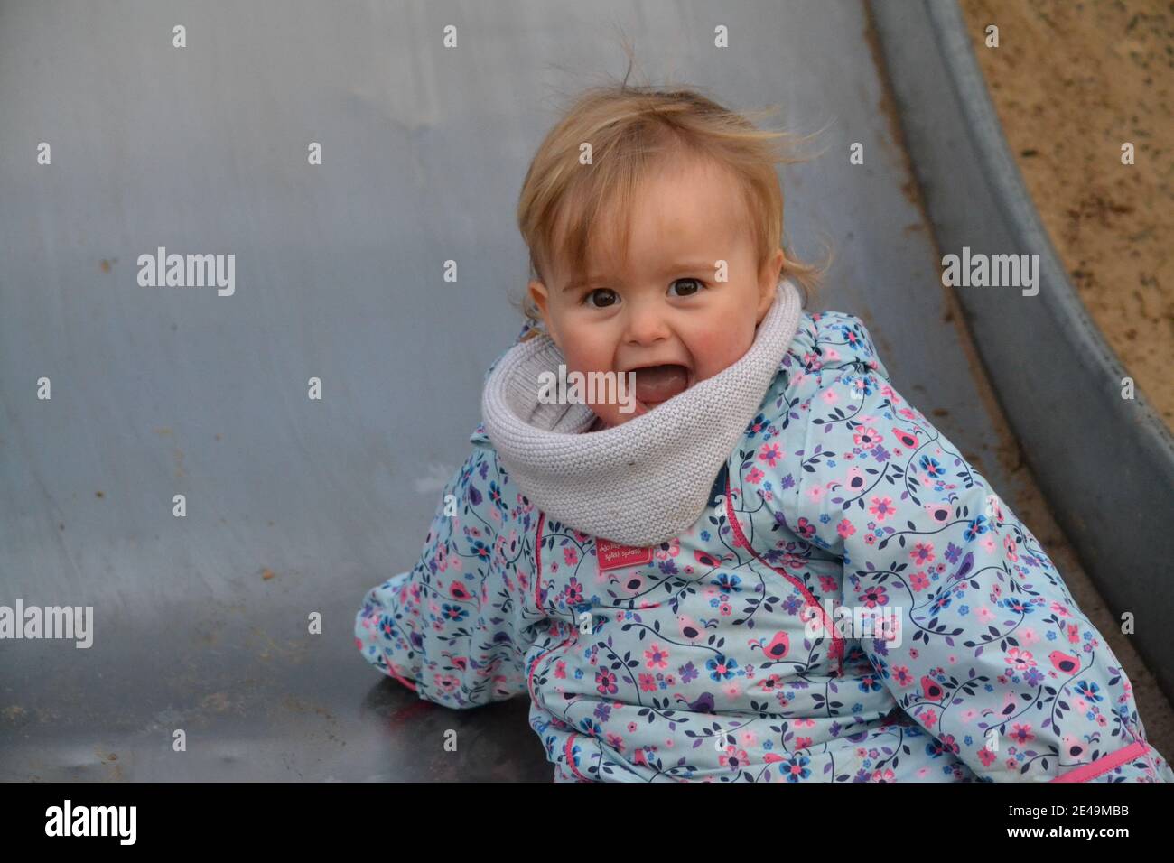 Young Girl Playing At The Park On The Slide - Big Smile - Winters Day - Toddler - Female - UK Stock Photo