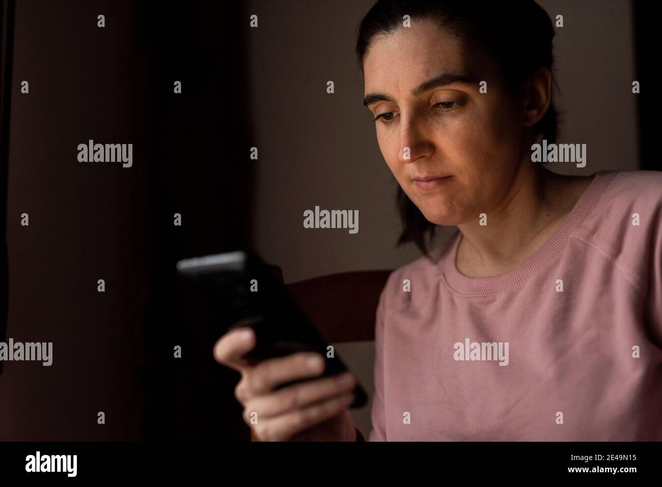 woman using mobile phone next to a window with natural light Stock Photo