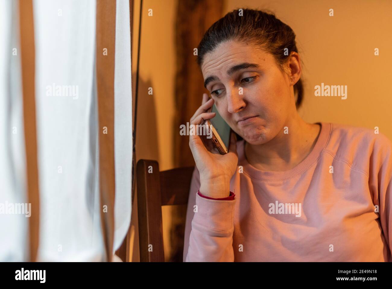 sad woman talking on the phone by a window Stock Photo