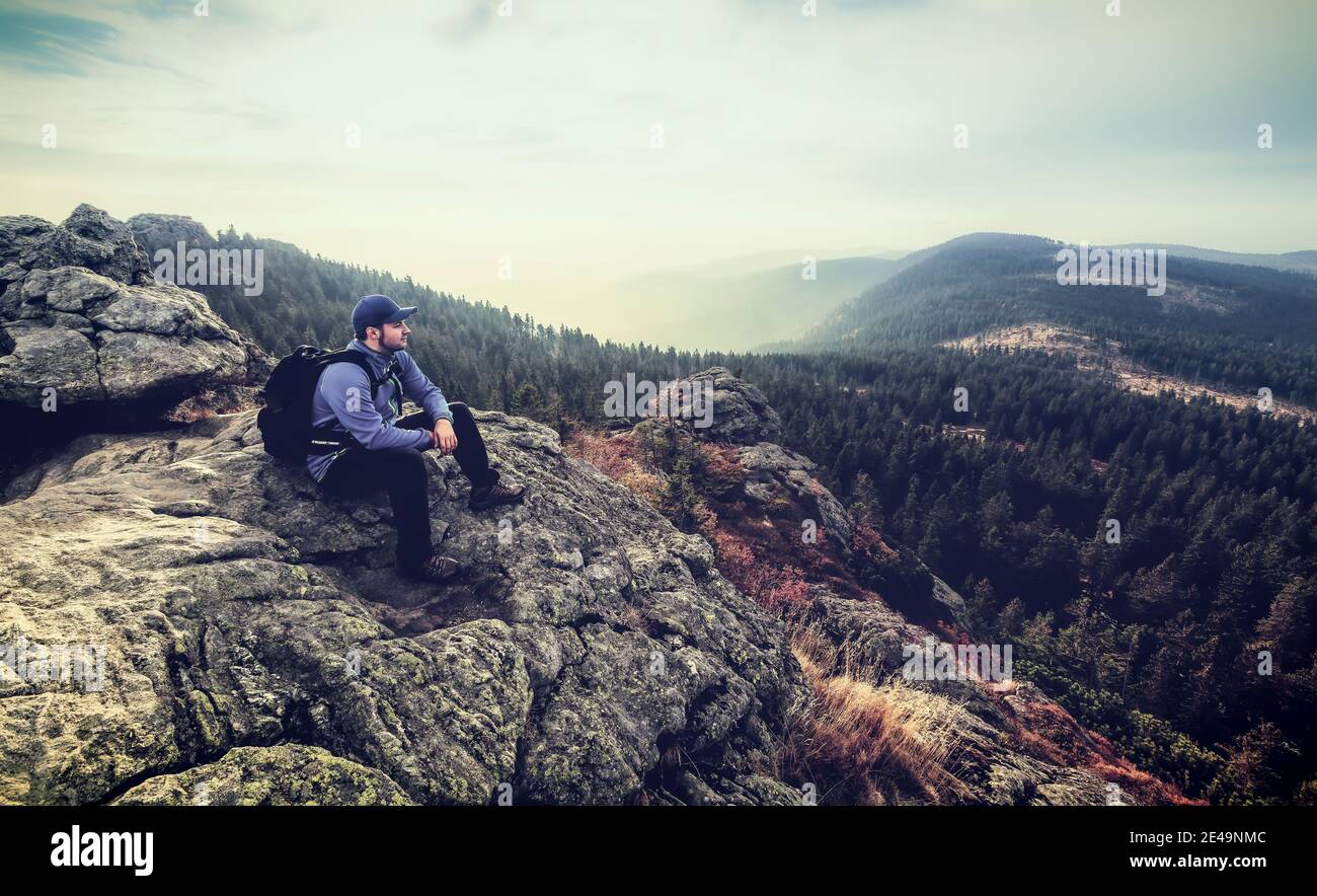 Man Hiker sitting on a rock at arriving peak and is looking into the far on top of großer Arber mountain located at National Park bavarian forest Stock Photo