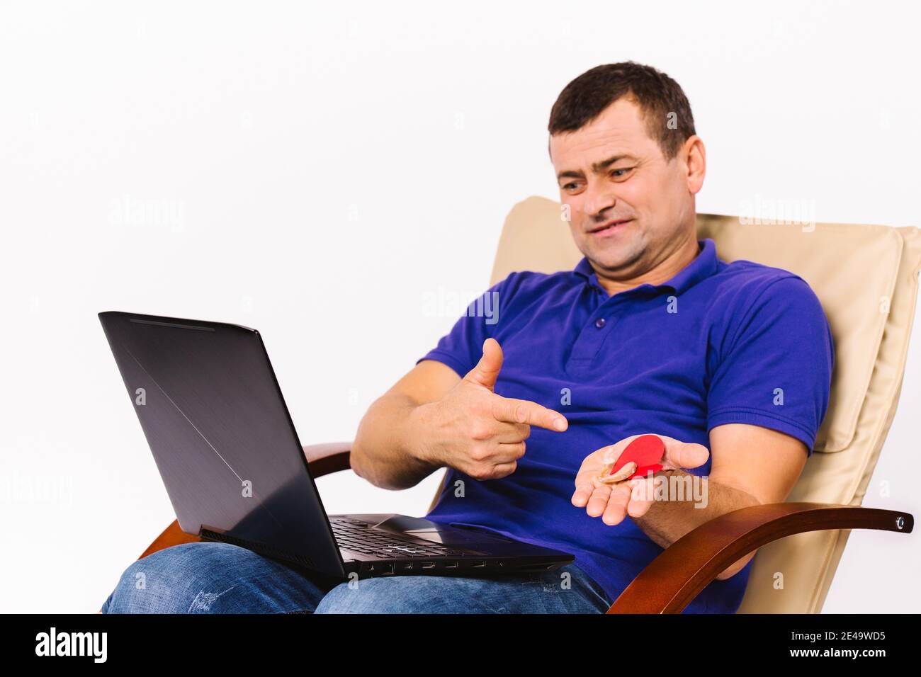 A surdomute man holds a hearing aid and a red heart in his hands while discuss by video communication via a laptop. Stock Photo