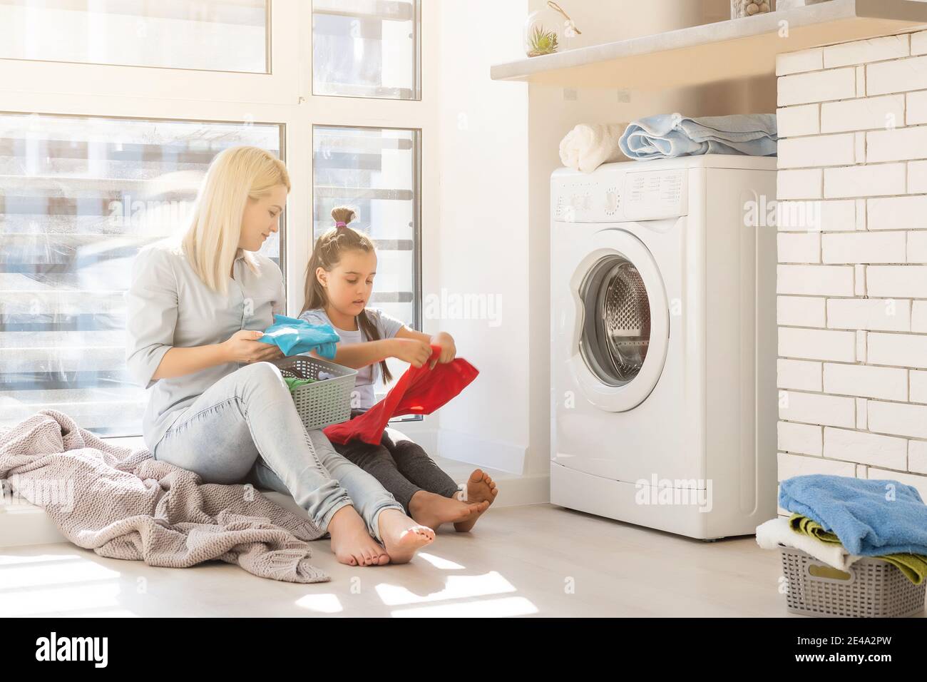 Happy housewife and her daughter with linen near washing machine Stock Photo