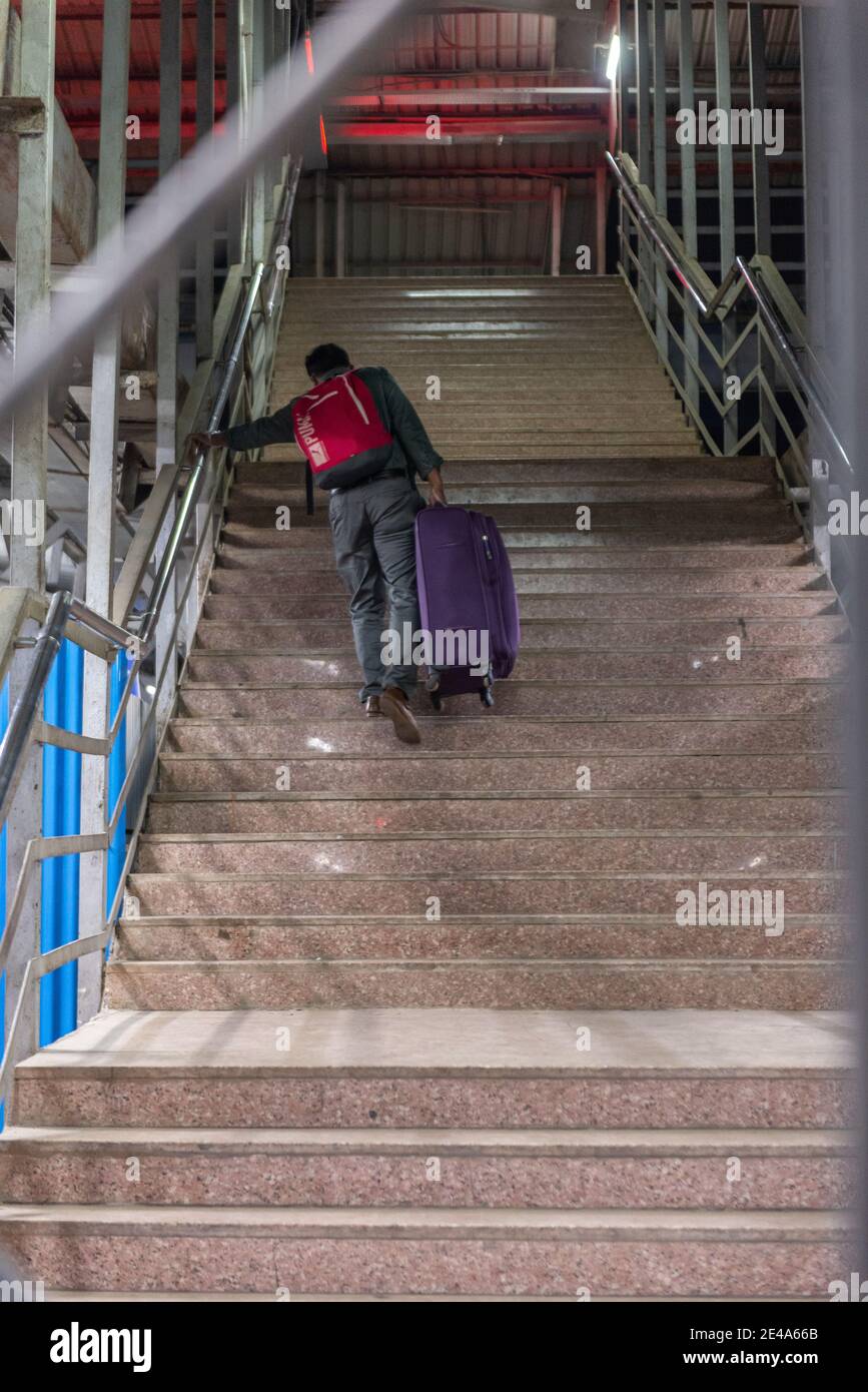 Man climbing stairs with heavy luggage at Vasai Road Railway Station, Maharashtra, India Stock Photo