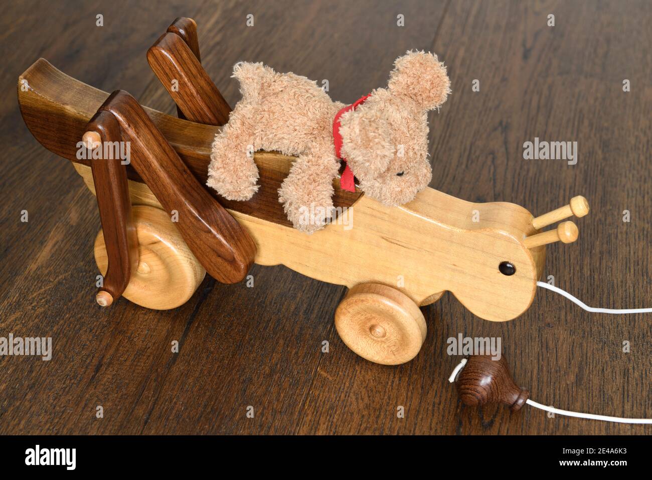 Handcrafted wood cricket with teddy bear riding up top on hardwood floor Stock Photo