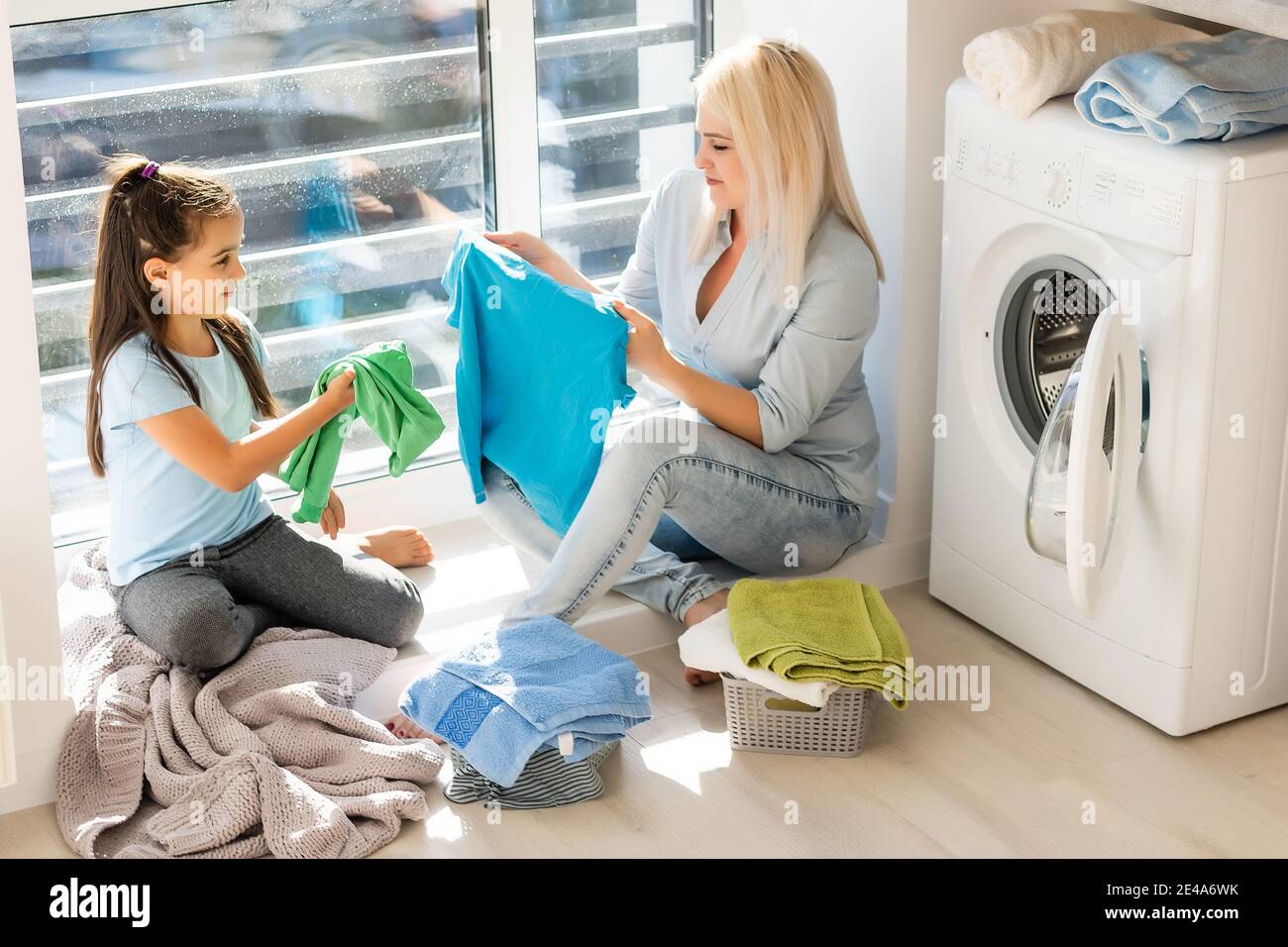 Happy housewife and her daughter with linen near washing machine Stock Photo