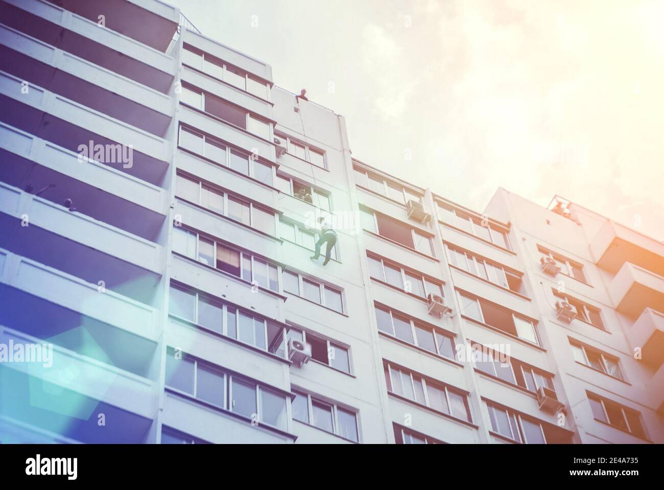 A man on a rope descends from the roof of a building on a rope through a window. Stock Photo
