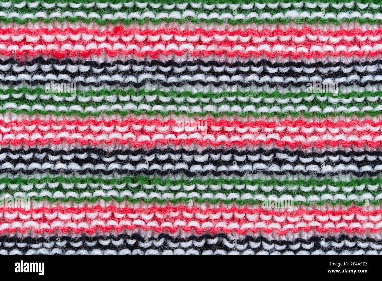 Close-up of hand made knitted stitch wool pattern in red, white, black and green. Stock Photo