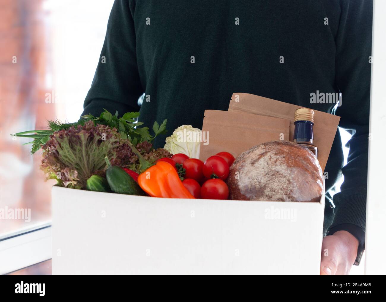 A person delivering box with farmer bio crop in the house doorway. Fresh organic greens and vegetables delivery. Small local business support. Stock Photo
