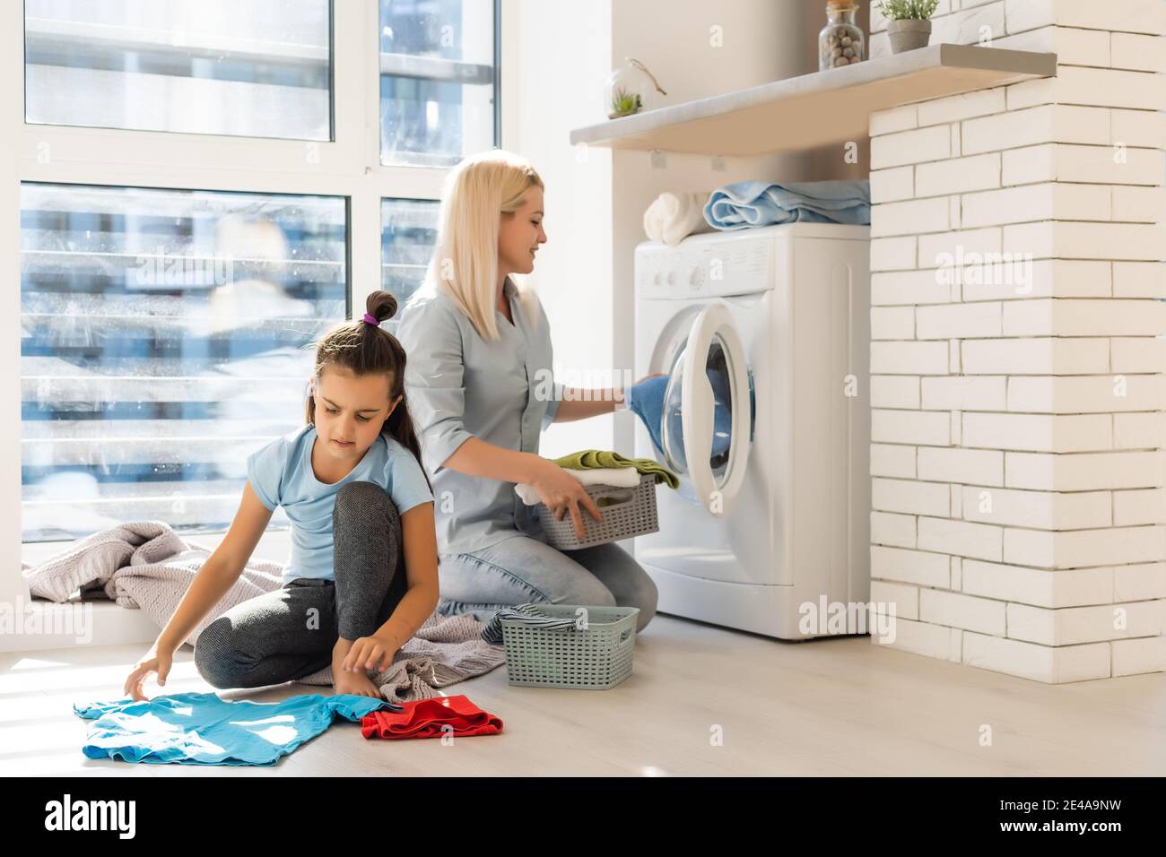 Happy housewife and her daughter with linen near washing machine Stock Photo