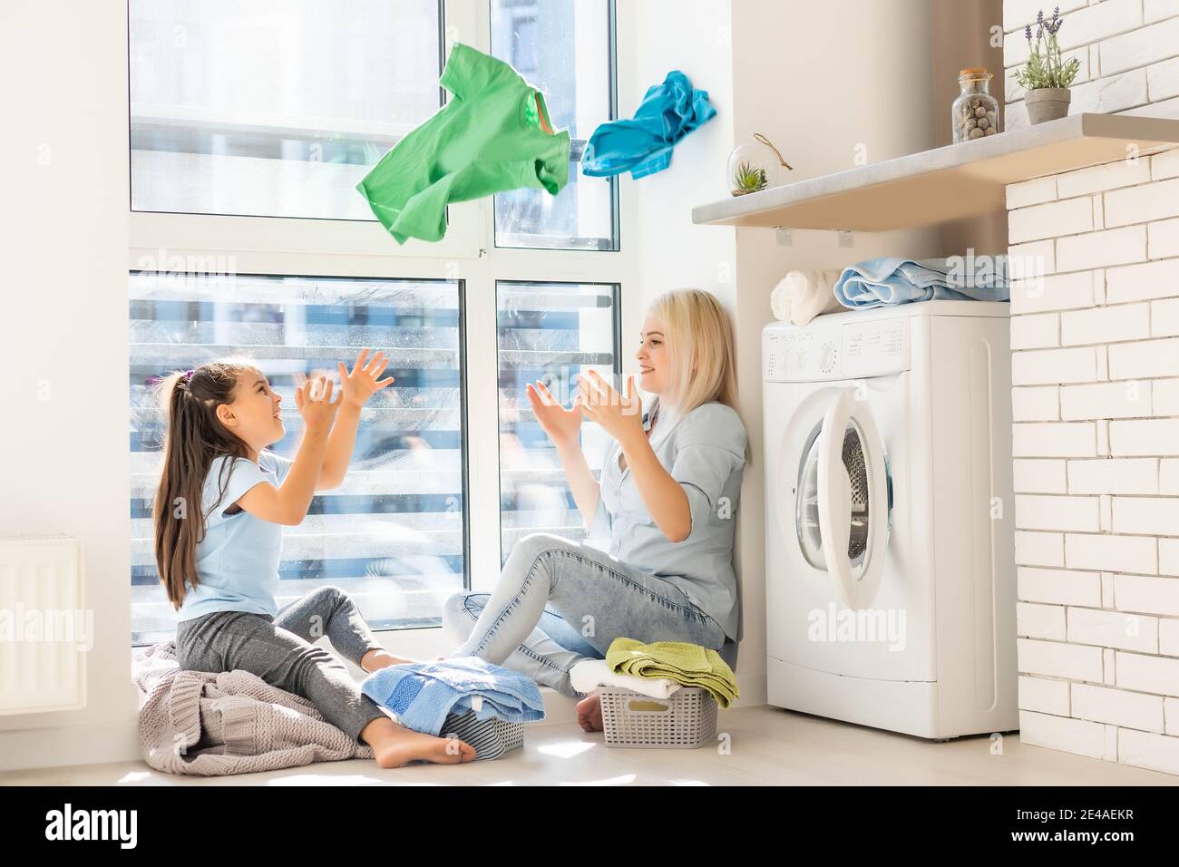 Happy housewife and her daughter with linen near washing machine Stock Photo
