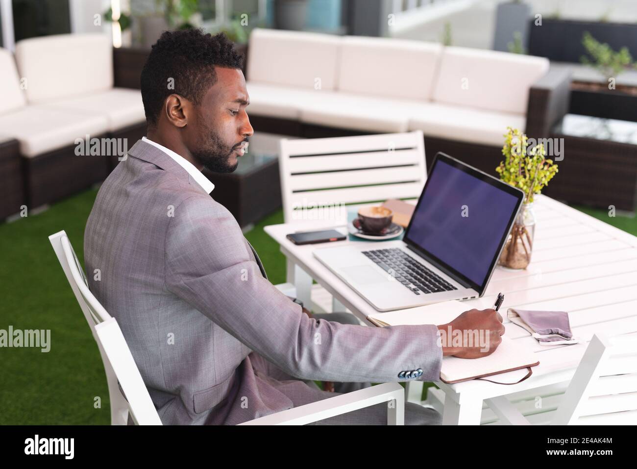 African american man sitting in a cafe using laptop and writing in ...
