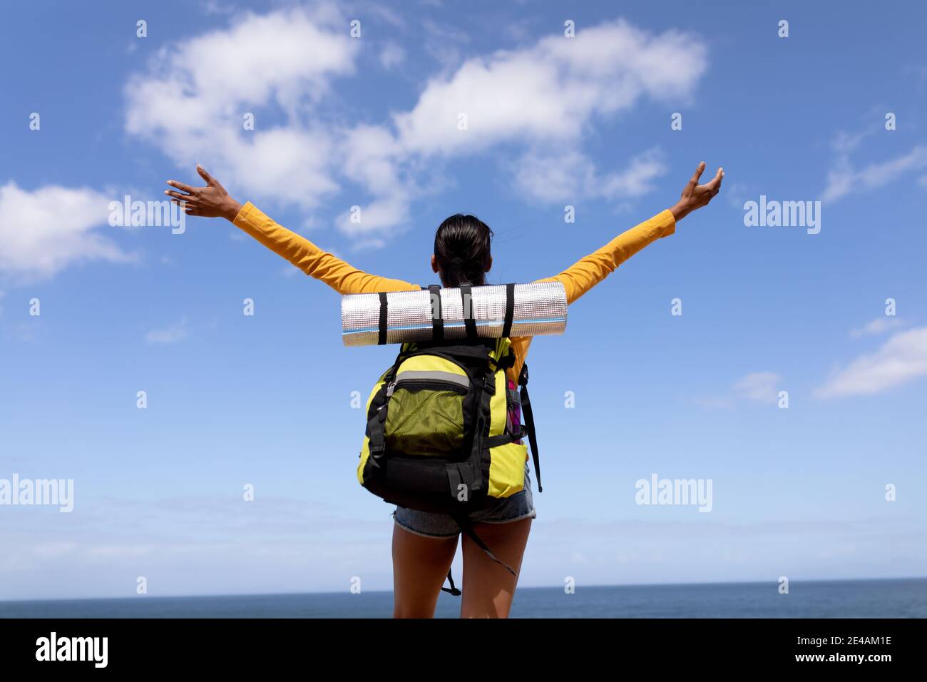 Fit afrcan american woman wearing backpack hiking spreading arms on the coast Stock Photo