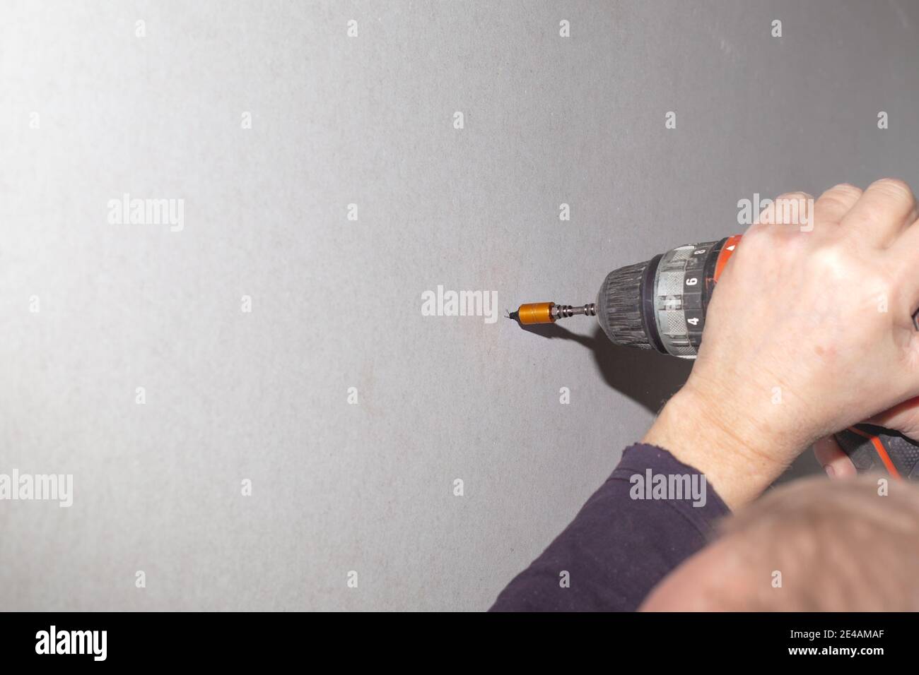 A man uses a screwdriver to screw a screw into a drywall. Home renovation, wall cladding. Stock Photo