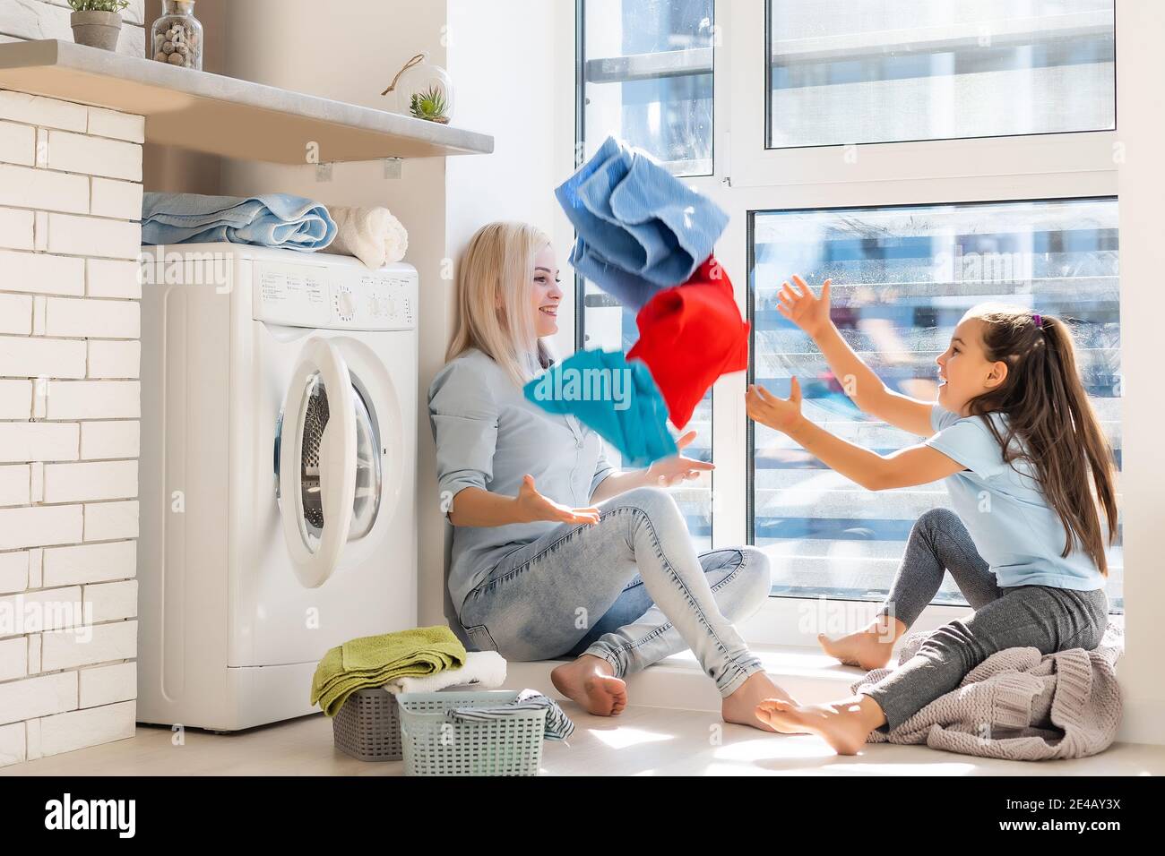 Happy housewife and her daughter with linen near washing machine Stock Photo