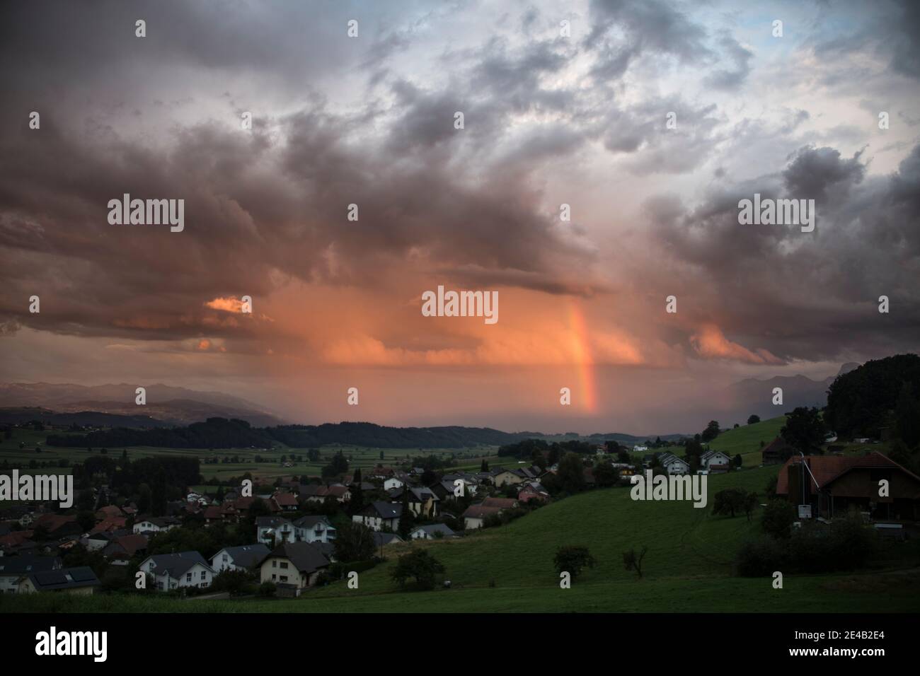 Village with a thunderstorm atmosphere with a rainbow, Thun region Stock Photo