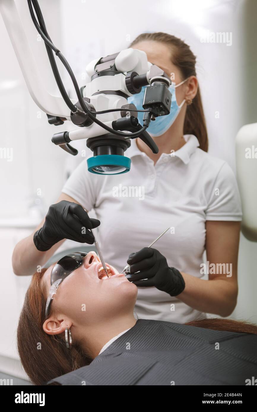 Professional dentist using dental microscope, working at her clinic Stock Photo