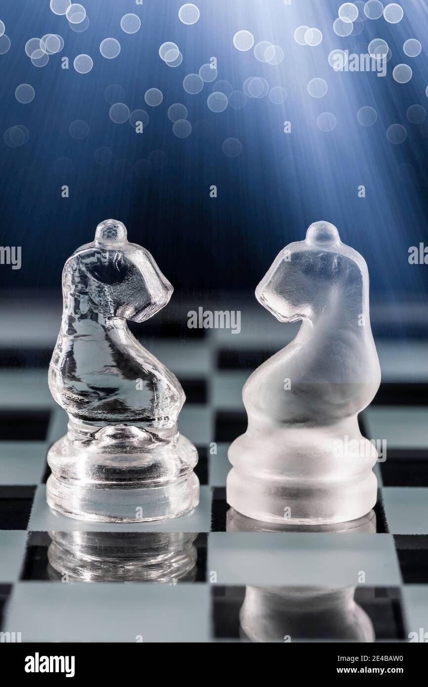 Glass chess pieces on a glass chessboard with reflection, on a blue background. Stock Photo