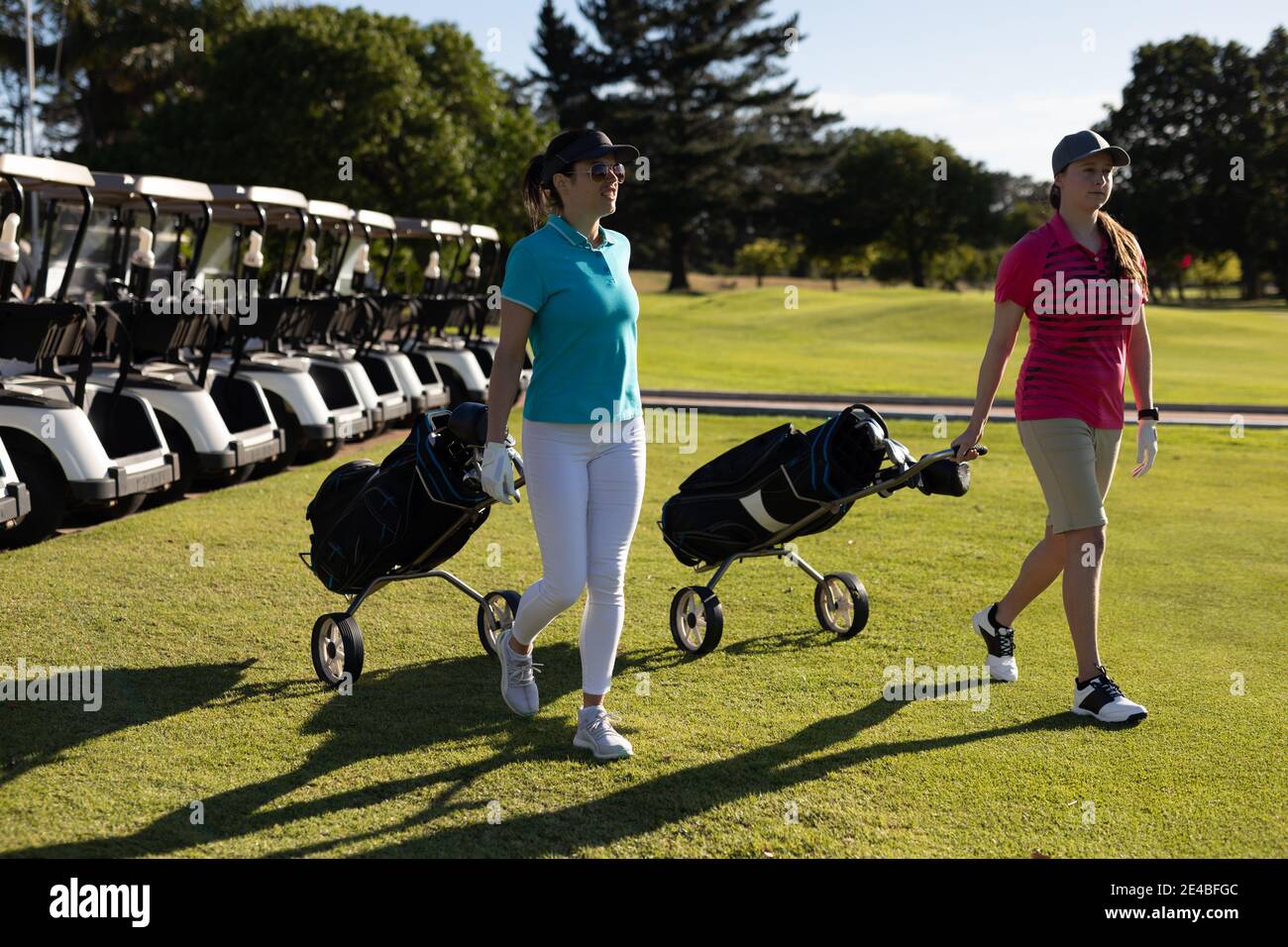 Two caucasian women walking across golf course pulling golf bags on wheels Stock Photo