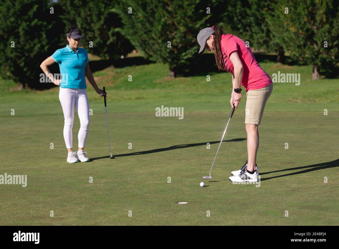 Two caucasian women playing golf one taking a shot at the hole Stock Photo