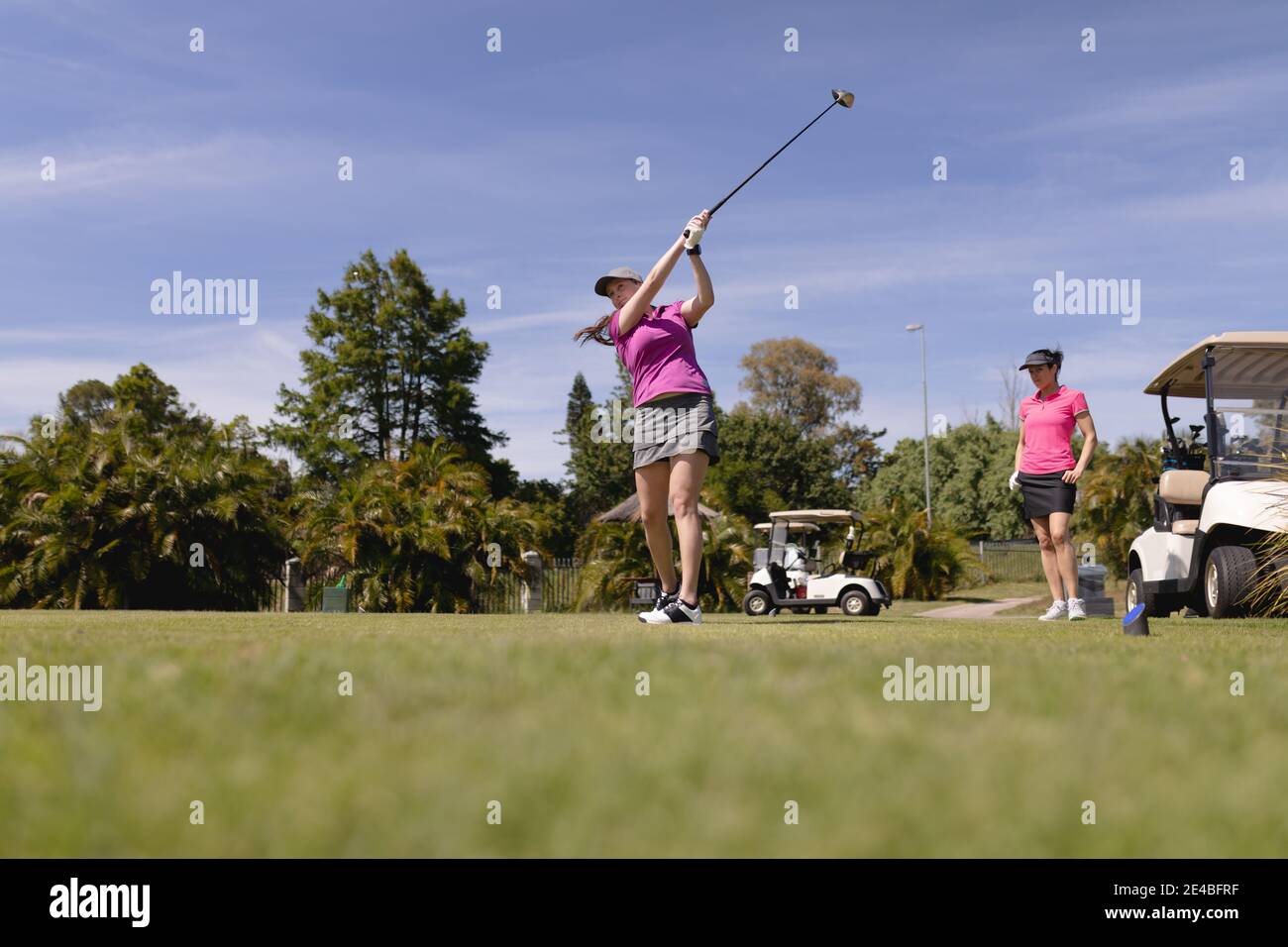 Two caucasian women playing golf one swinging club and taking a shot Stock Photo