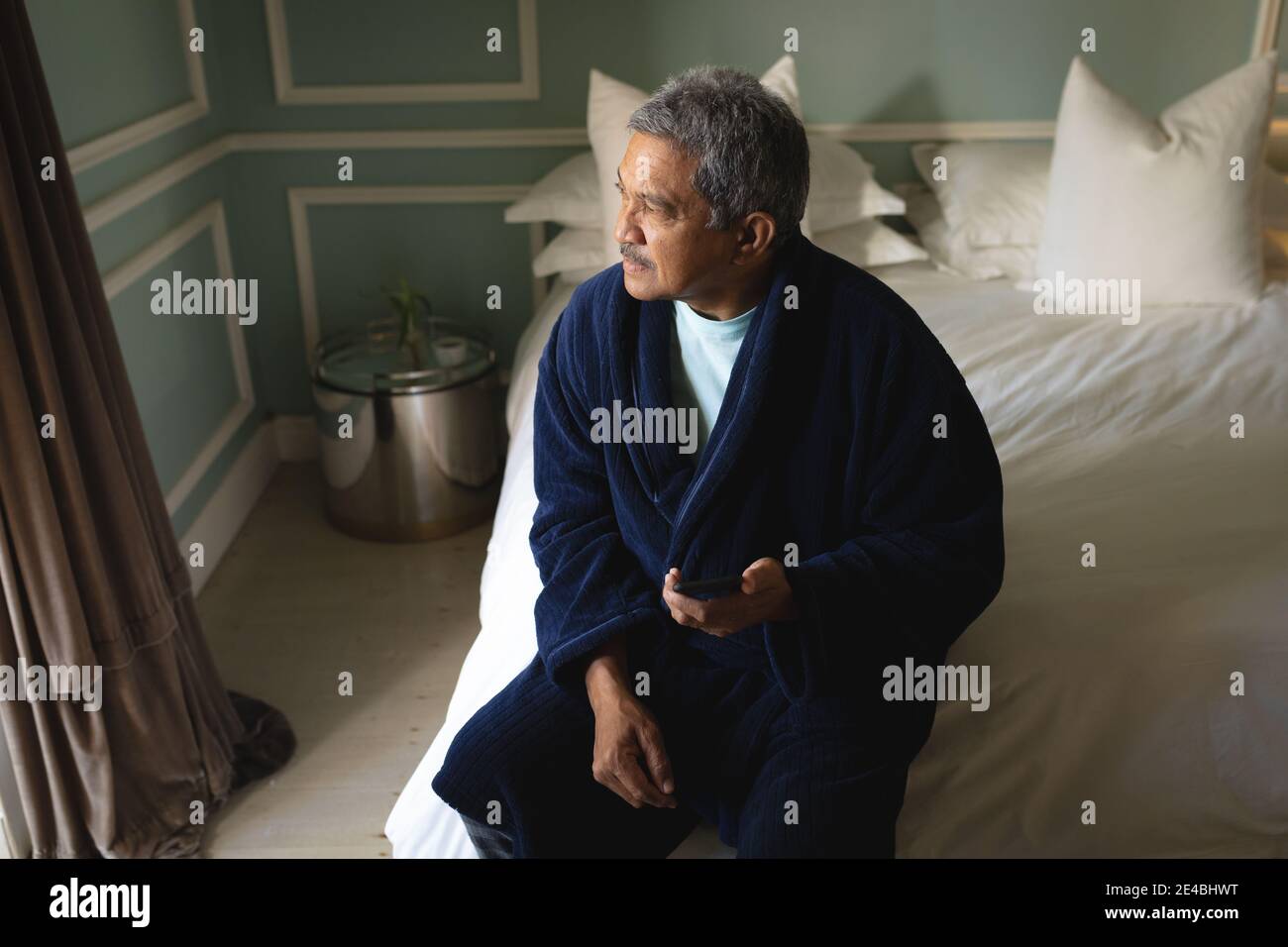 Senior african american man sitting on a bed using smartphone in a sleeping room Stock Photo