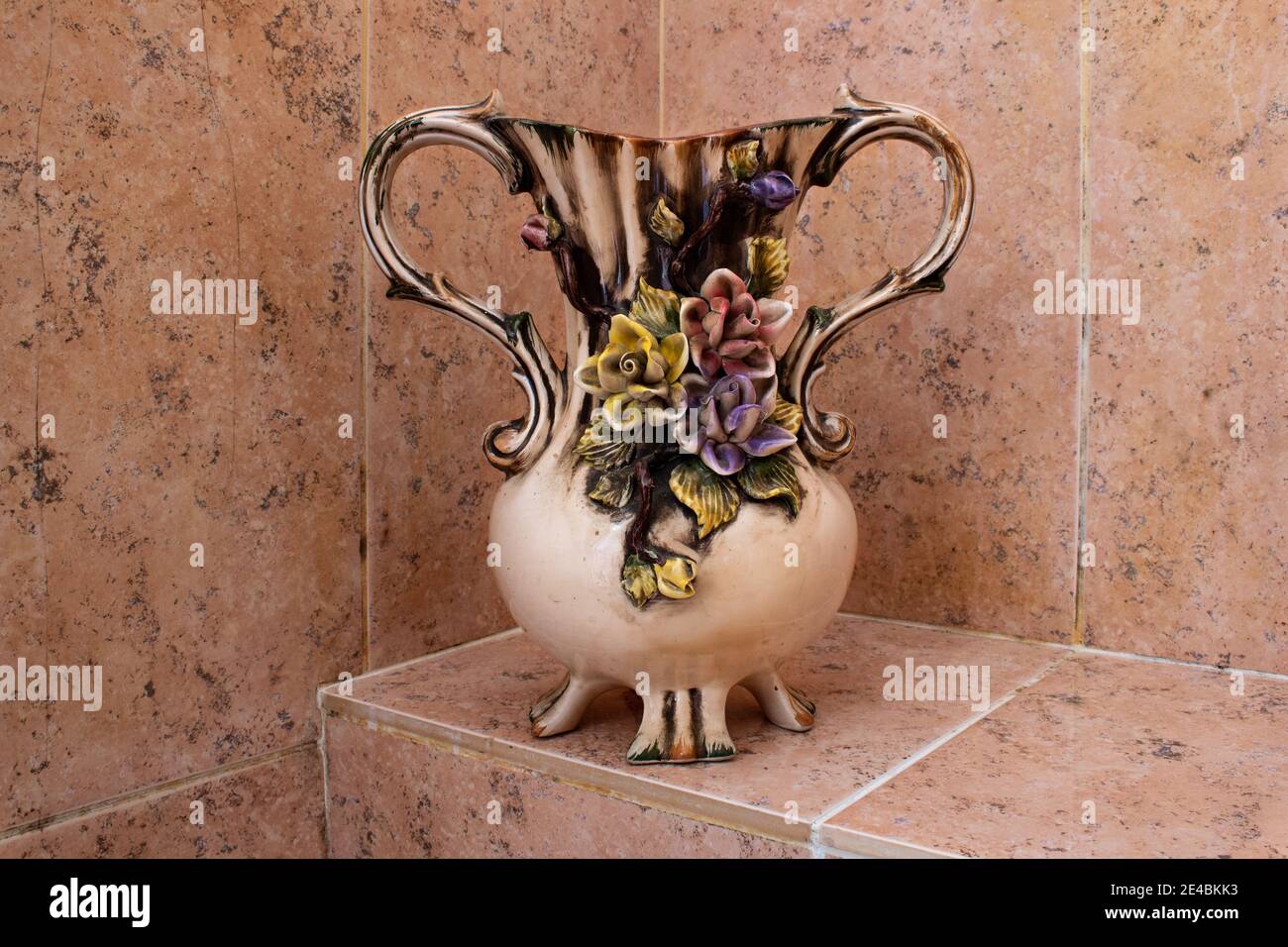Old vintage pottery jar with embossed colorful flowers standing on a tile step. Salmon colors Stock Photo