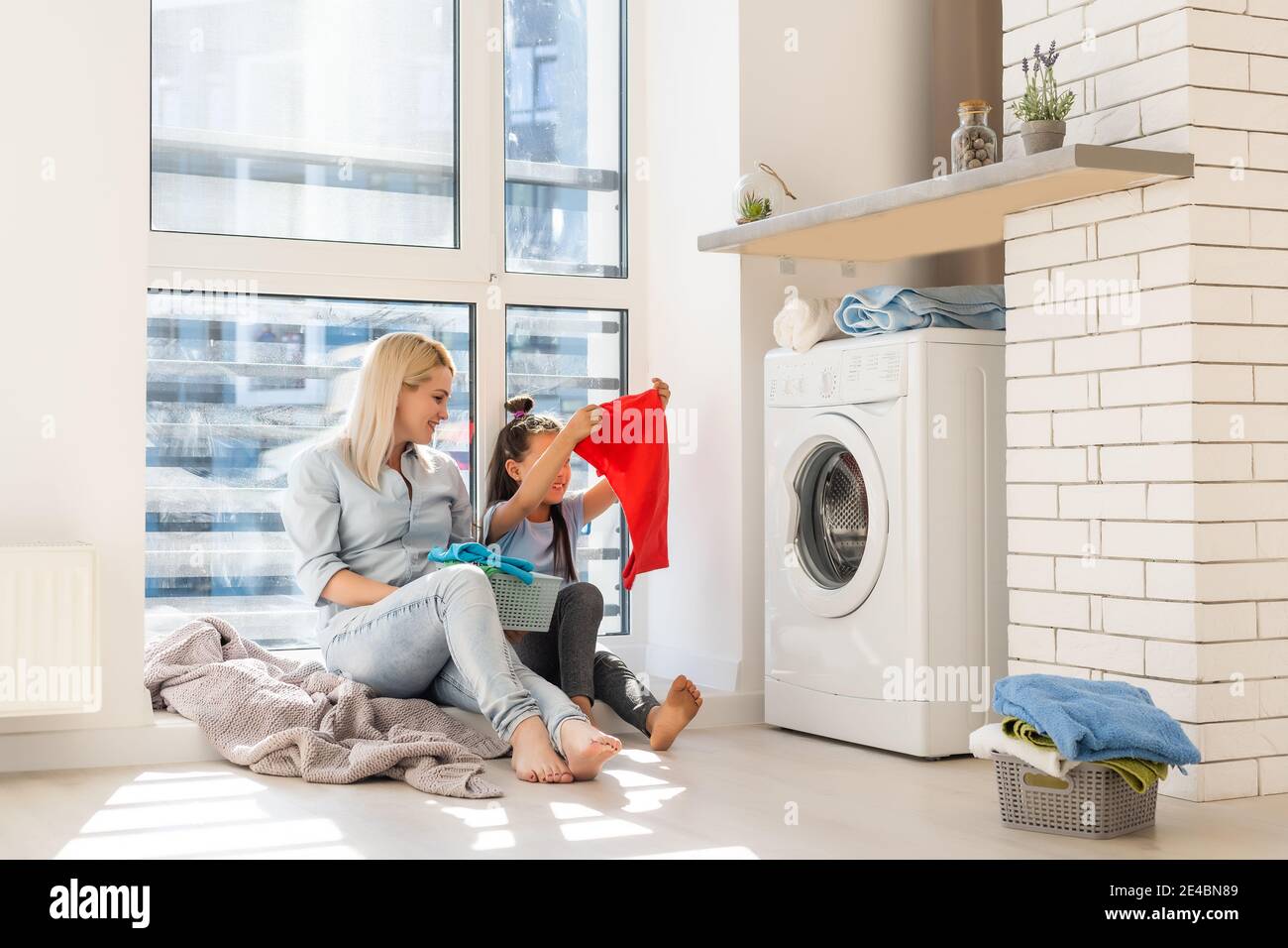 Happy housewife and her daughter with linen near washing machine Stock Photo