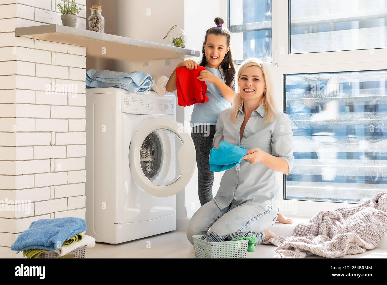 Happy housewife and her daughter with linen near washing machine Stock Photo