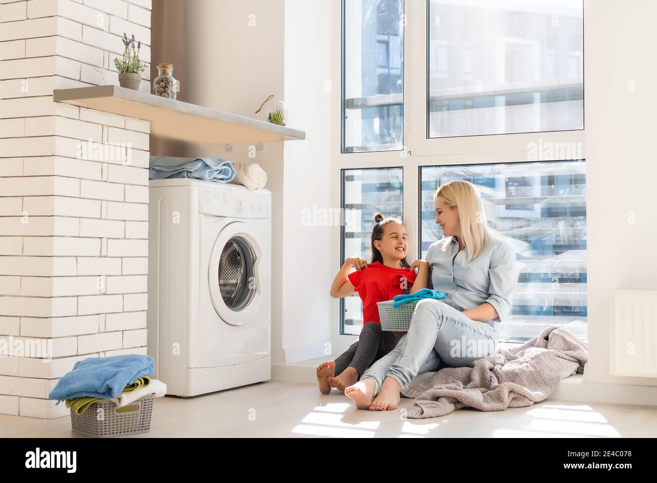 Happy housewife and her daughter with linen near washing machine Stock Photo