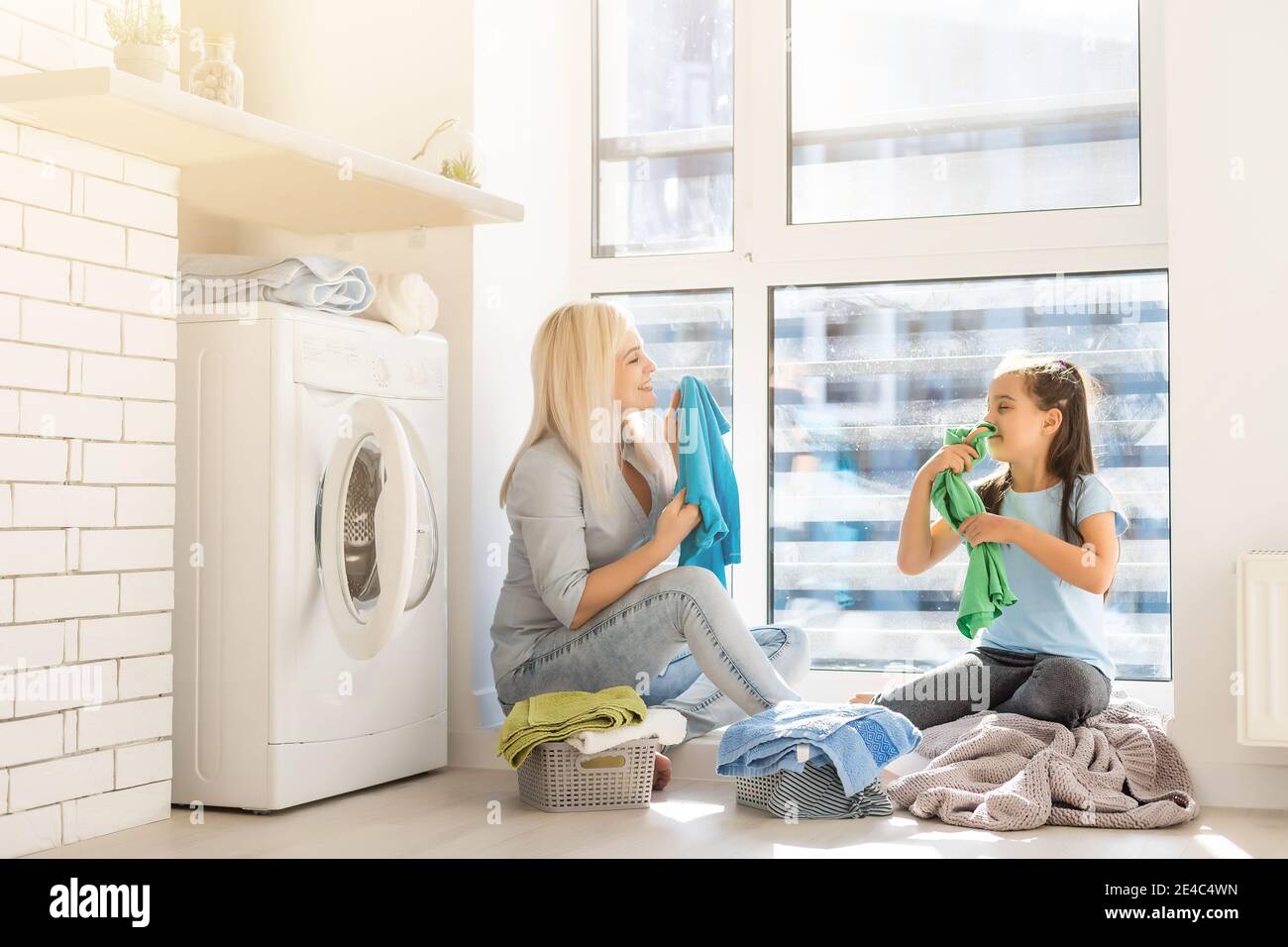 Happy housewife and her daughter with linen near washing machine Stock Photo