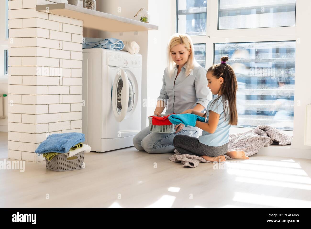Happy housewife and her daughter with linen near washing machine Stock Photo