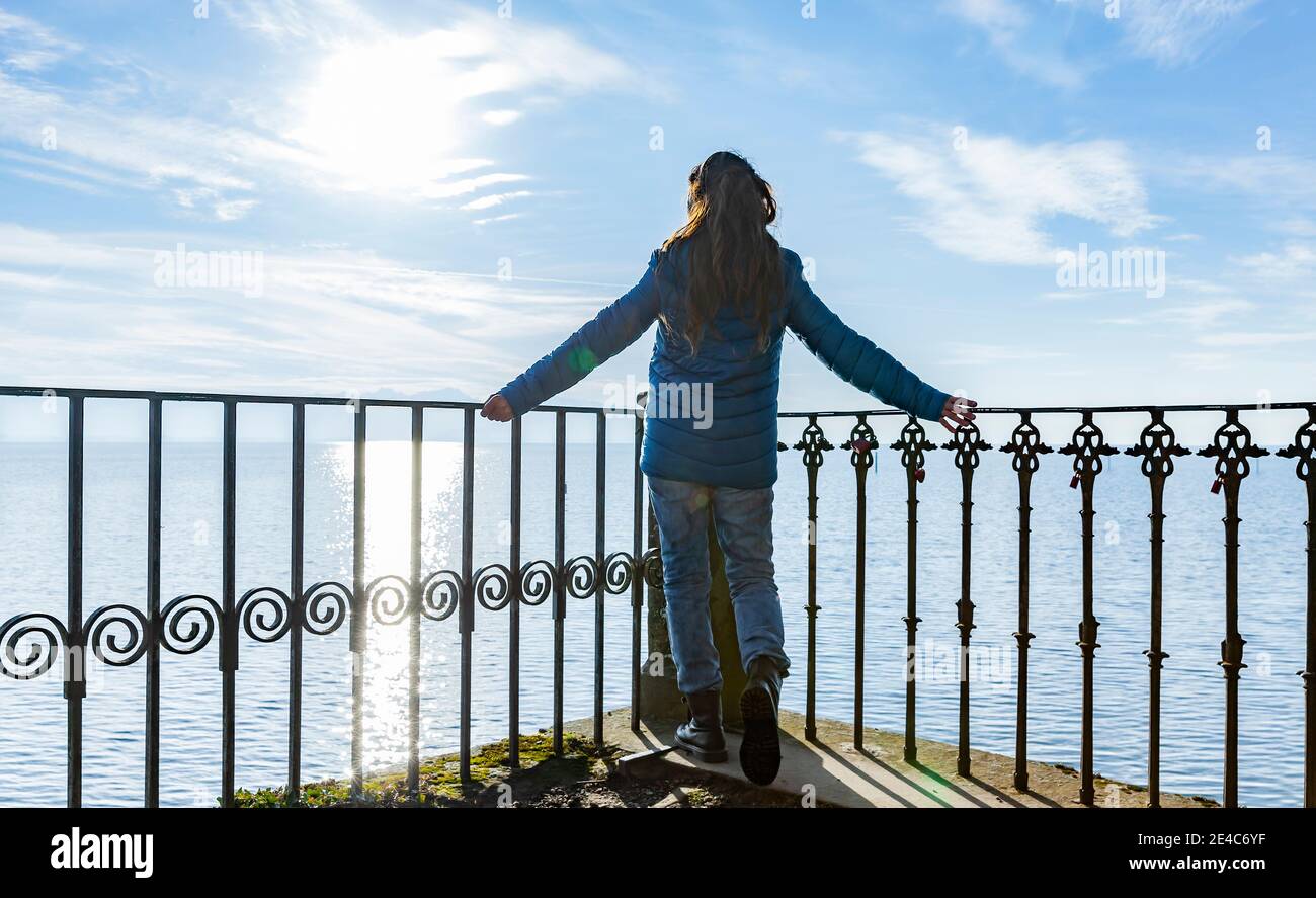 Woman in a blue down jacket on the railing by a lake Stock Photo