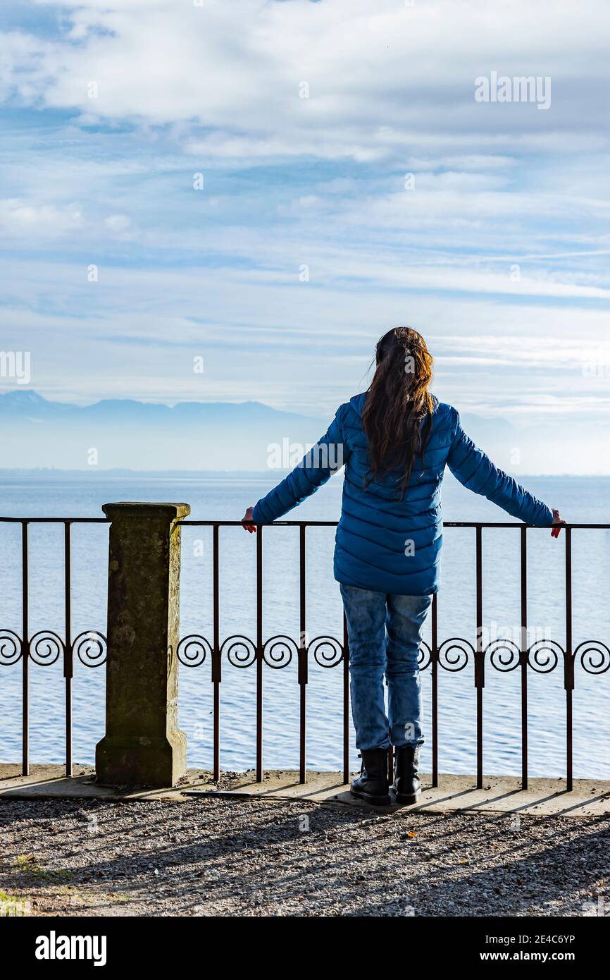 Woman in a blue down jacket on the railing by a lake Stock Photo