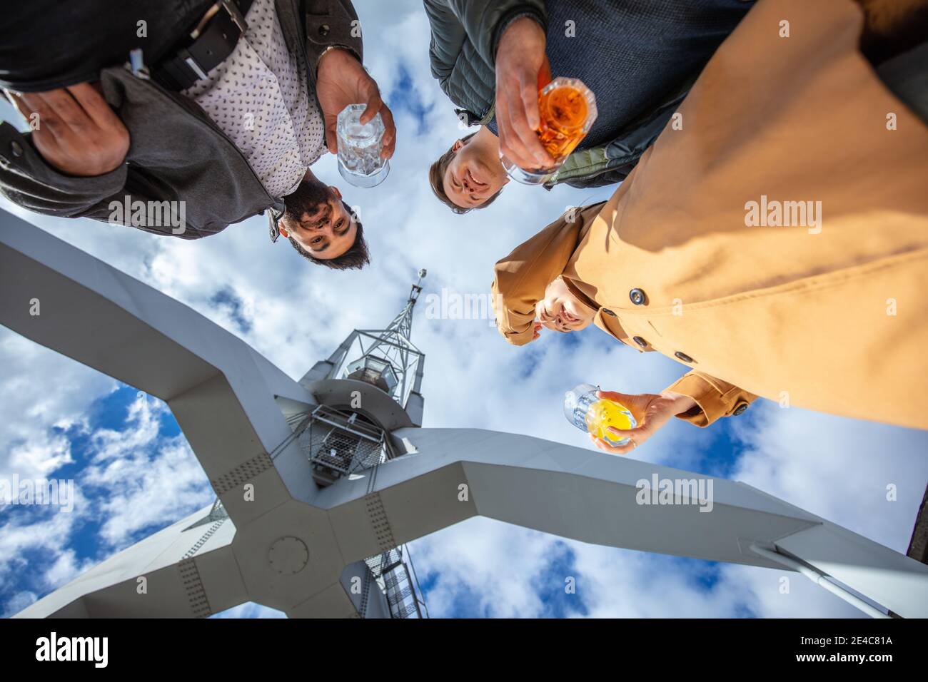 Young people, leisure time in the city. Three people stand at the harbor together with a drink in hand. View of the group from a frog's perspective Stock Photo