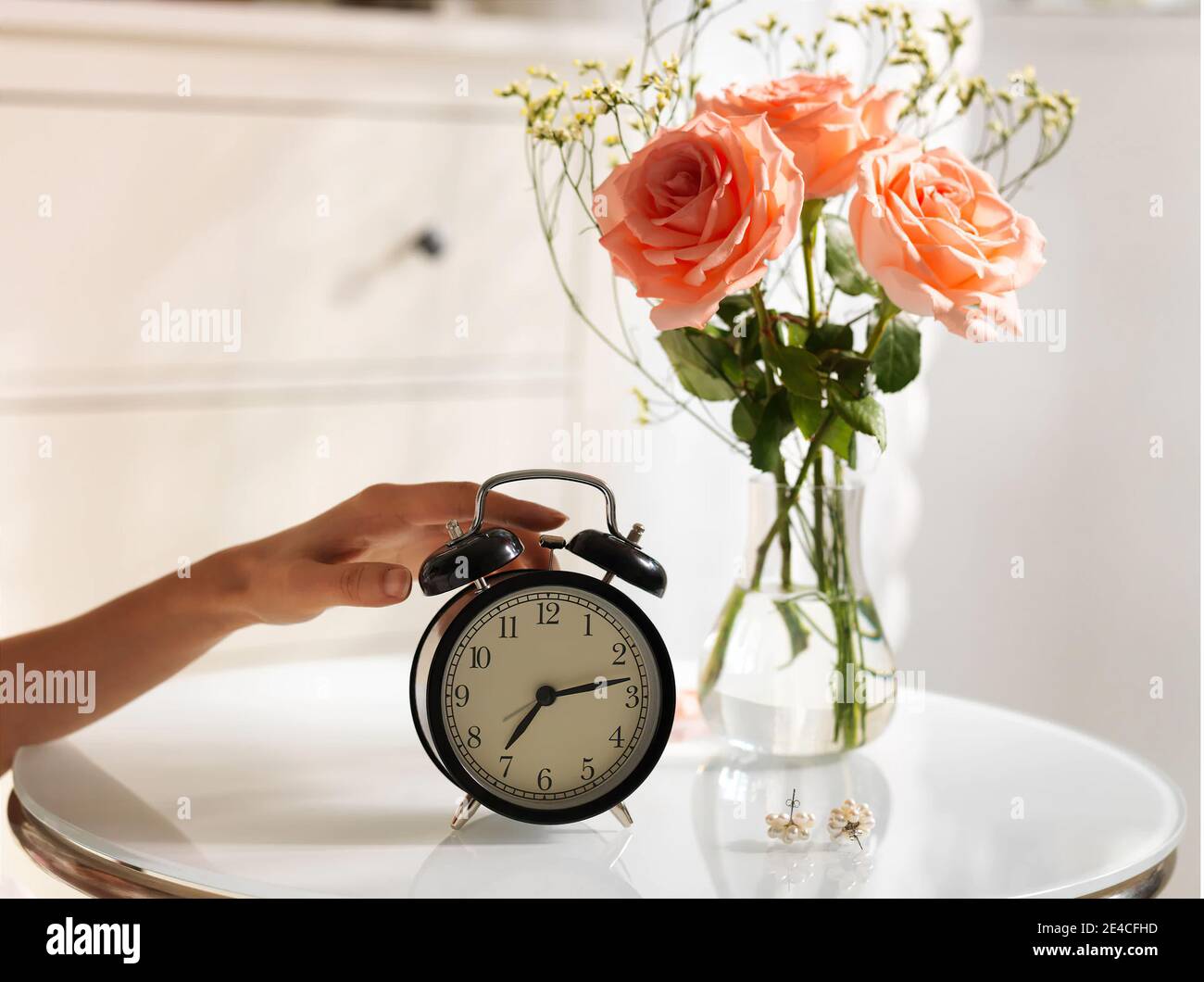 White Retro Alarm Clock in the bedroom on the table with roses in a