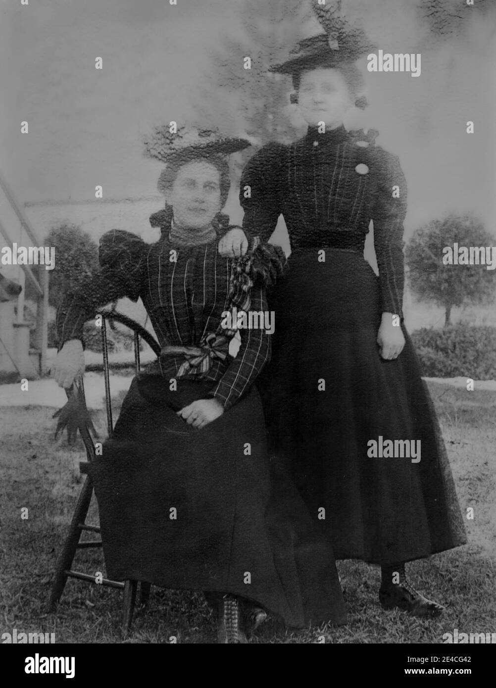 American archive monochrome portrait  of two women wearing matching tartan outfits in a garden. One young woman is standing and one woman is seated on a chair.. Taken in the late 19th century in Port Byron, NY, USA Stock Photo