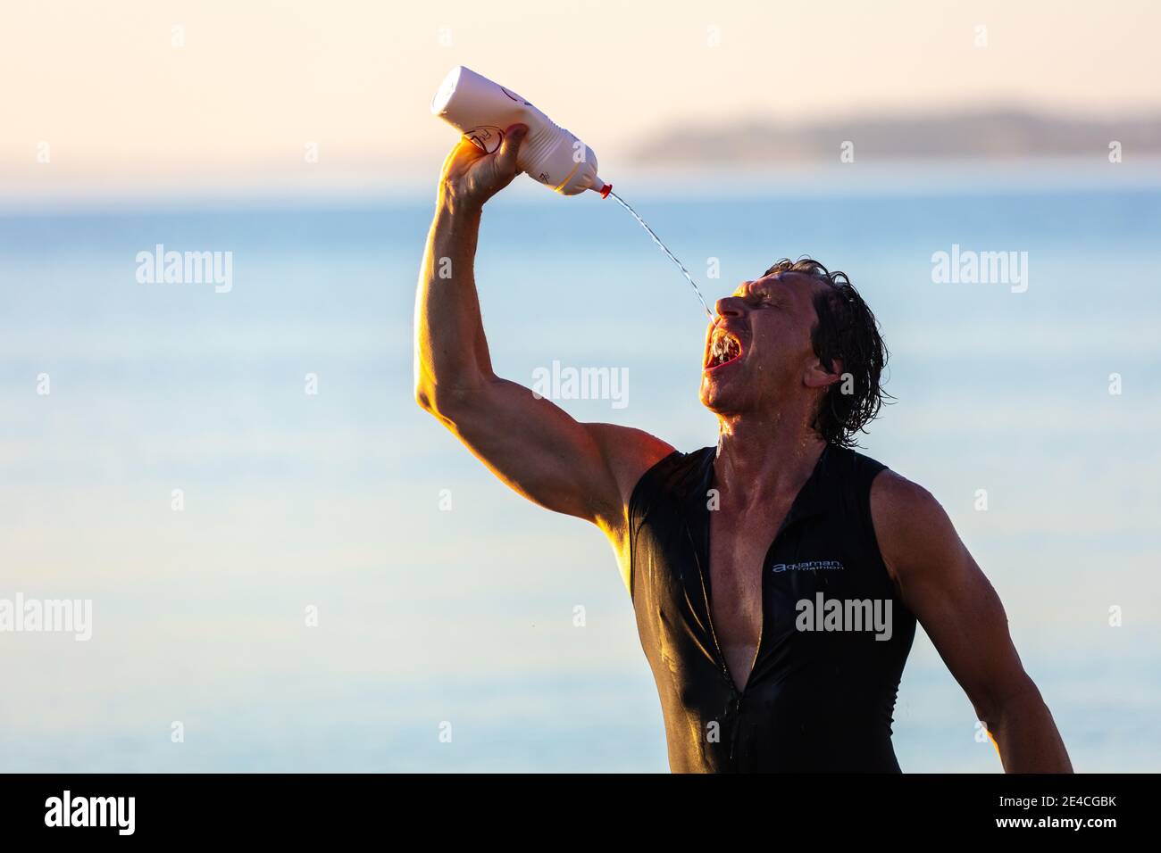 Man 50 plus fit, with a wetsuit in the sea, drinks from his water bottle. Stock Photo