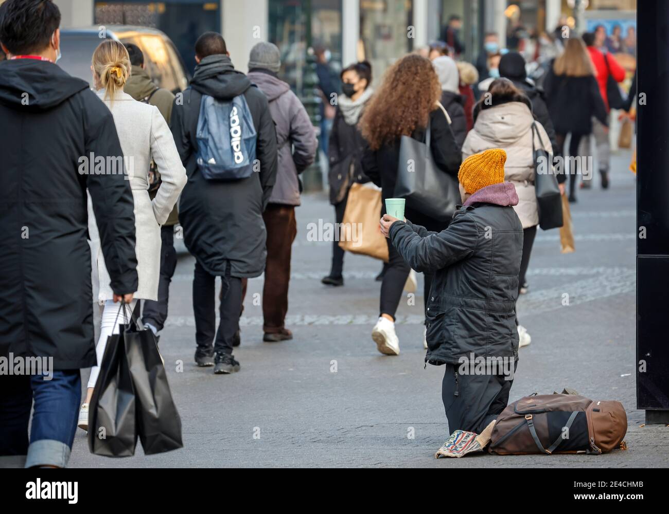 Duesseldorf, North Rhine-Westphalia, Germany - Beggar sits on the pavement in Düsseldorf's old town in times of the corona crisis during the second part of lockdown at Christmas time in the pedestrian zone, many passers-by with shopping bags go by. Stock Photo