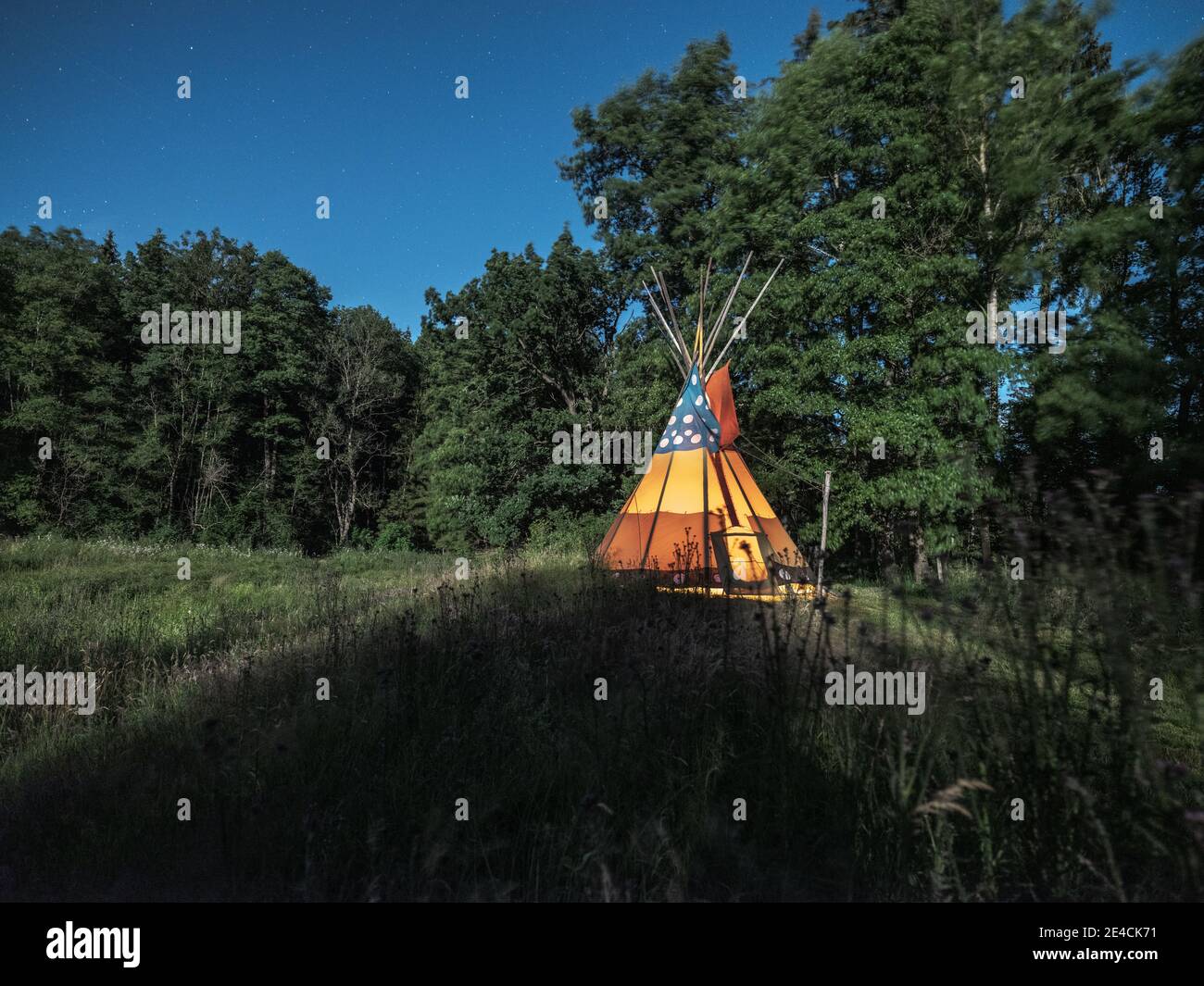 Tipi with fire on a meadow at night in the moonlight Stock Photo