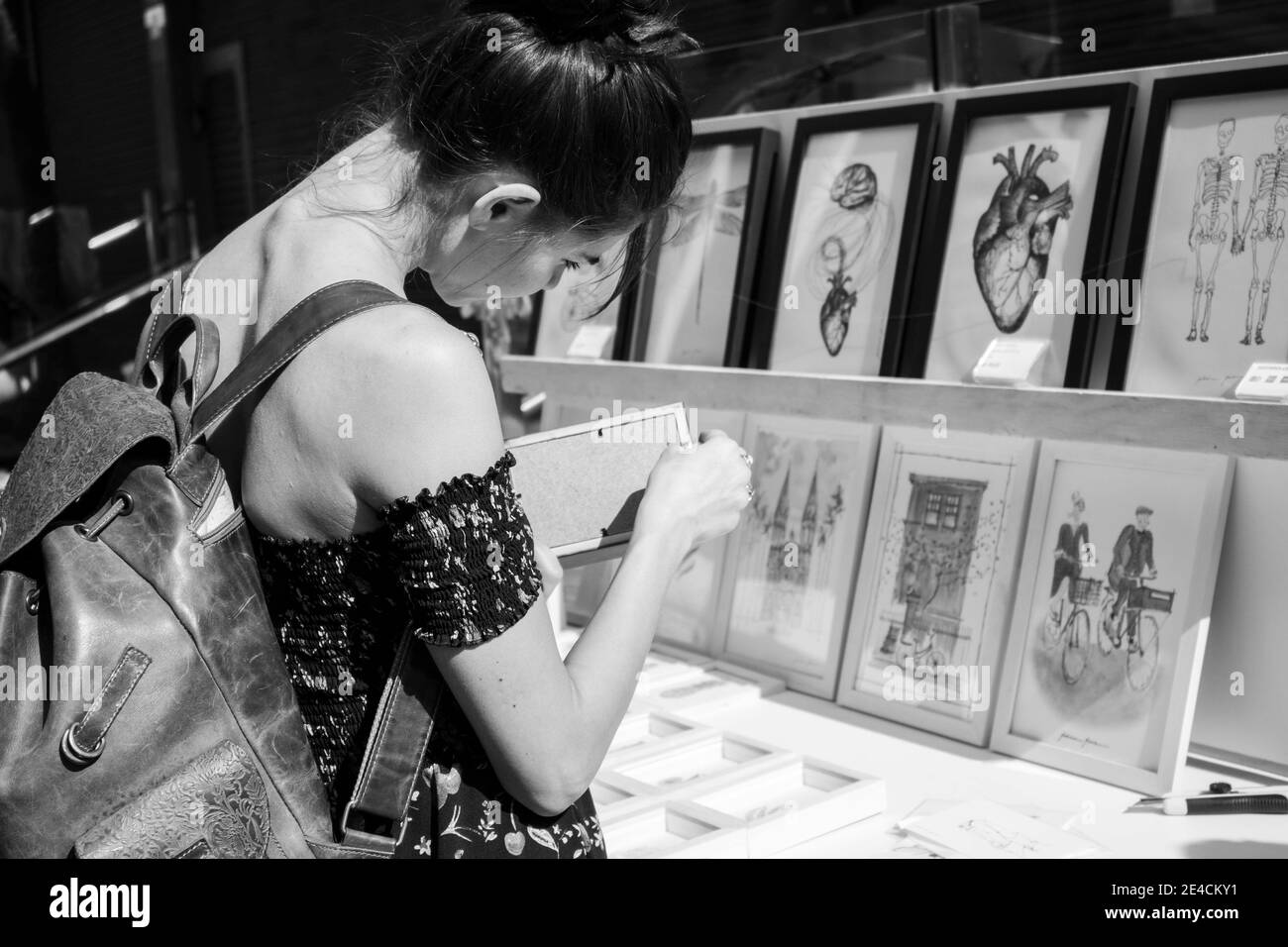 São Paulo / São Paulo / Brazil - 08 19 2018: Pretty exotic tropical woman choosing a drawing or a painting to buy at a market place. [Black and White] Stock Photo