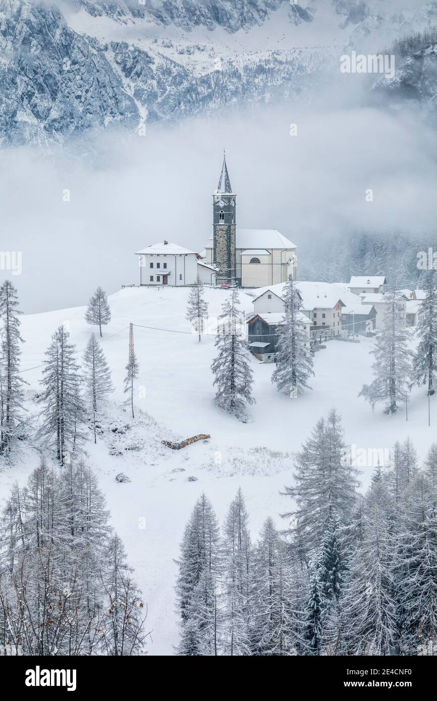 Italy, Veneto, province of Belluno, Rocca Pietore, Agordino, the village of Laste in winter with the church of San Gottardo on the hill, Dolomites Stock Photo
