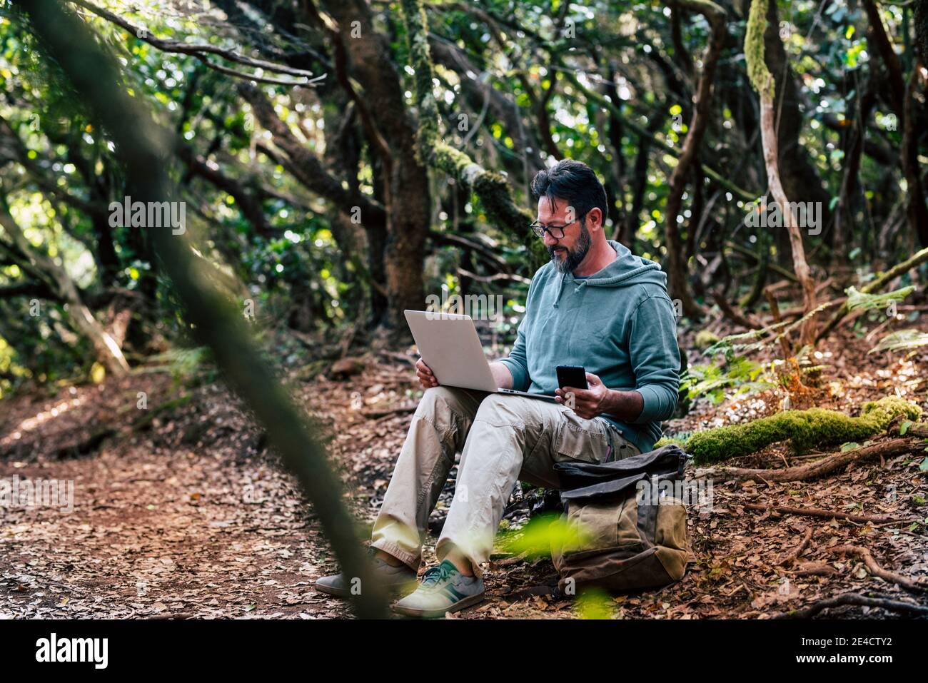 Adult young man work with online roaming connection technology outdoor with phone and laptop computer - people in nature outdoors alternative office with free job - digital nomad lifestyle Stock Photo