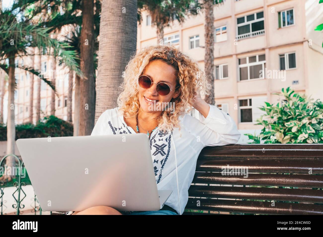 Cheerful beautiful lady work outdoor at the park with laptop computer sitting ona bench enjoying nature and freedom from office - concept of smart working and online job everywhere with connection Stock Photo