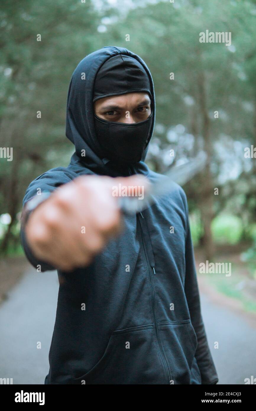 close up of thief in a mask with a knife wearing black hoodie pointed ...