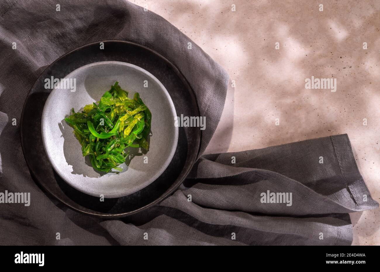 Green wakame seaweed Japanese salad over two plates and a grey napkin with copy space Stock Photo
