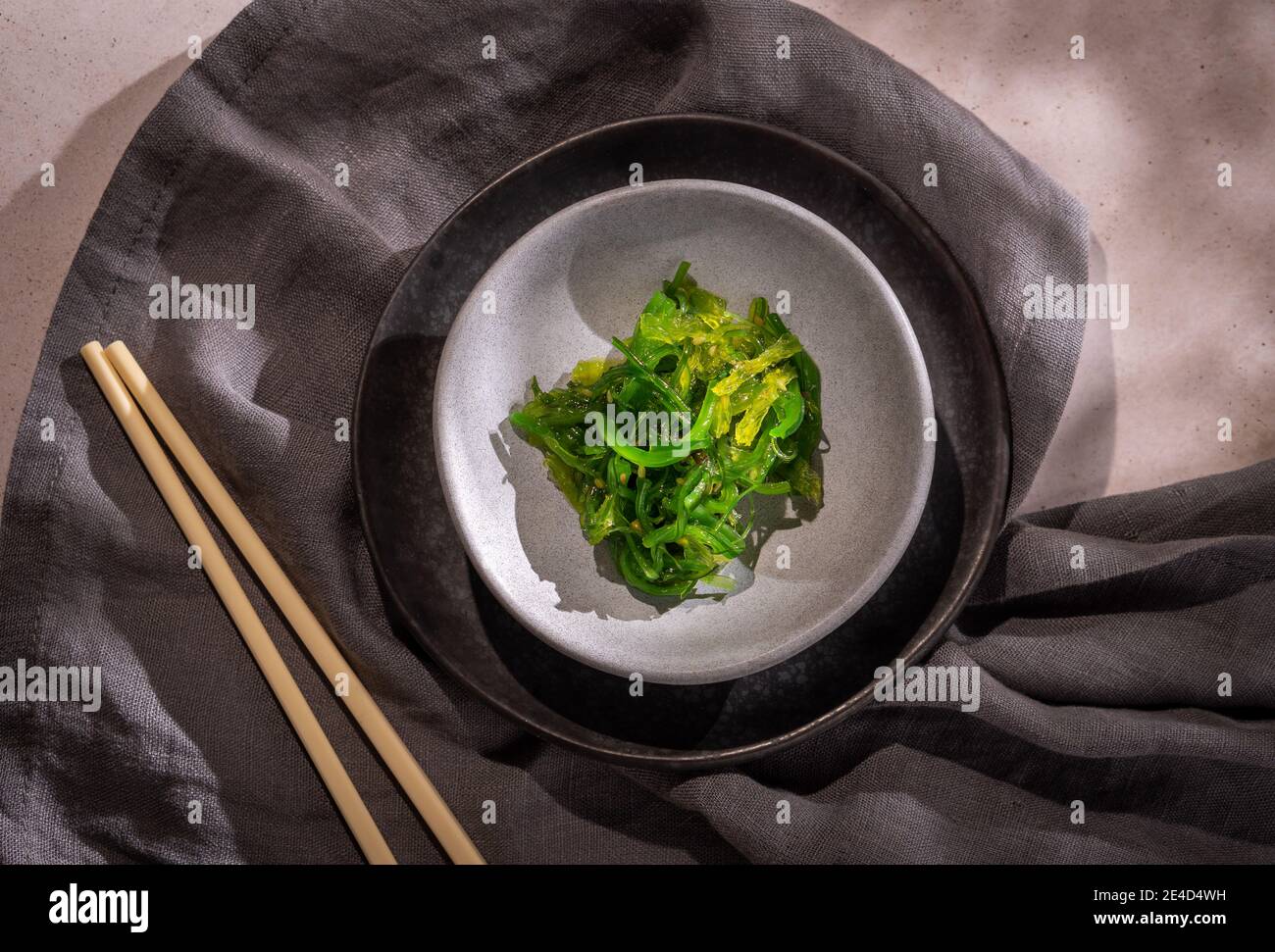 Green wakame seaweed Japanese salad over two plates, a grey napkin and a pair of chopsticks Stock Photo